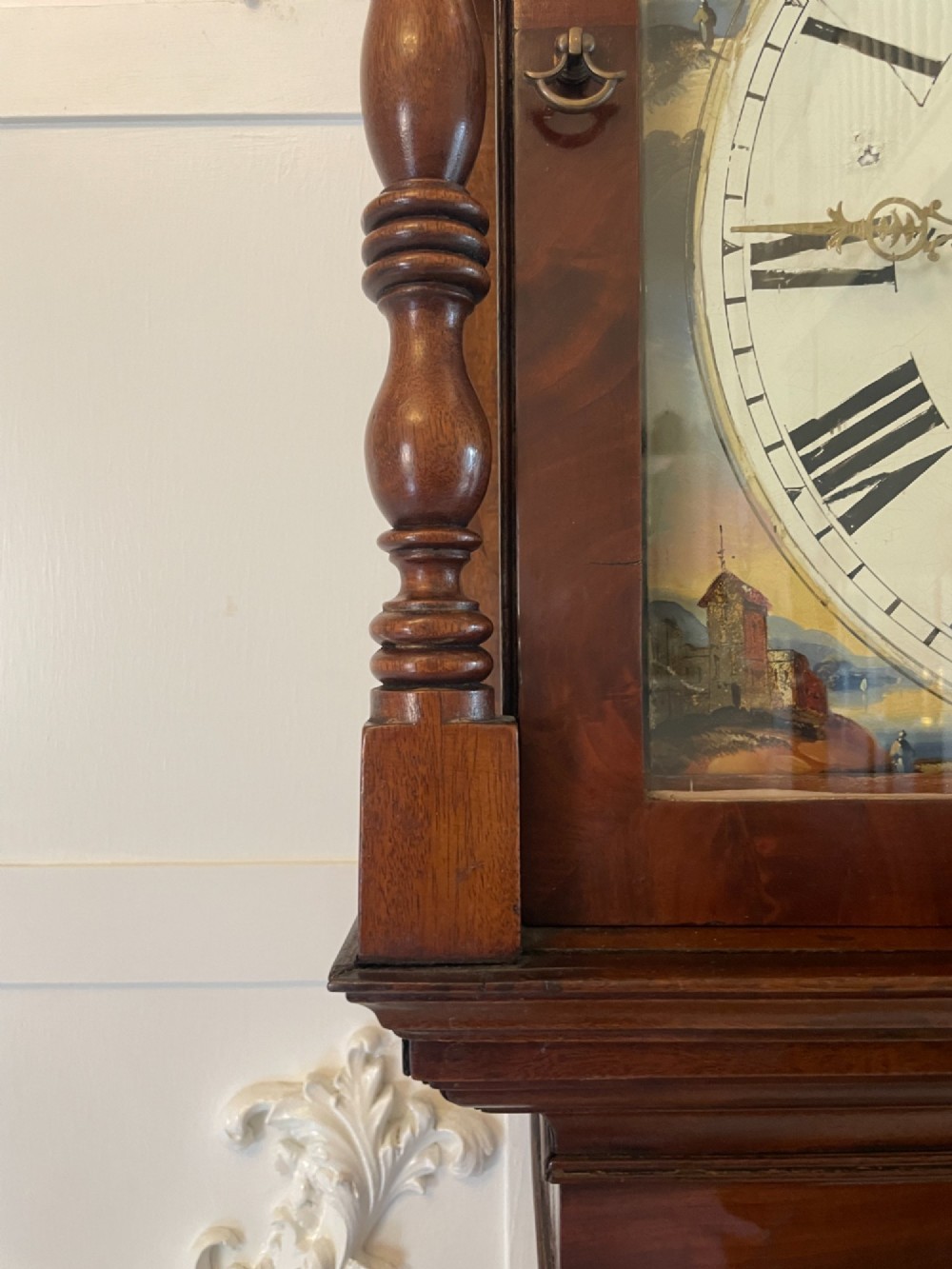 A George III flame mahogany longcase clock featuring a swan-neck pediment, turned hood columns, a painted arch dial, and a gothic-arched trunk door. View X