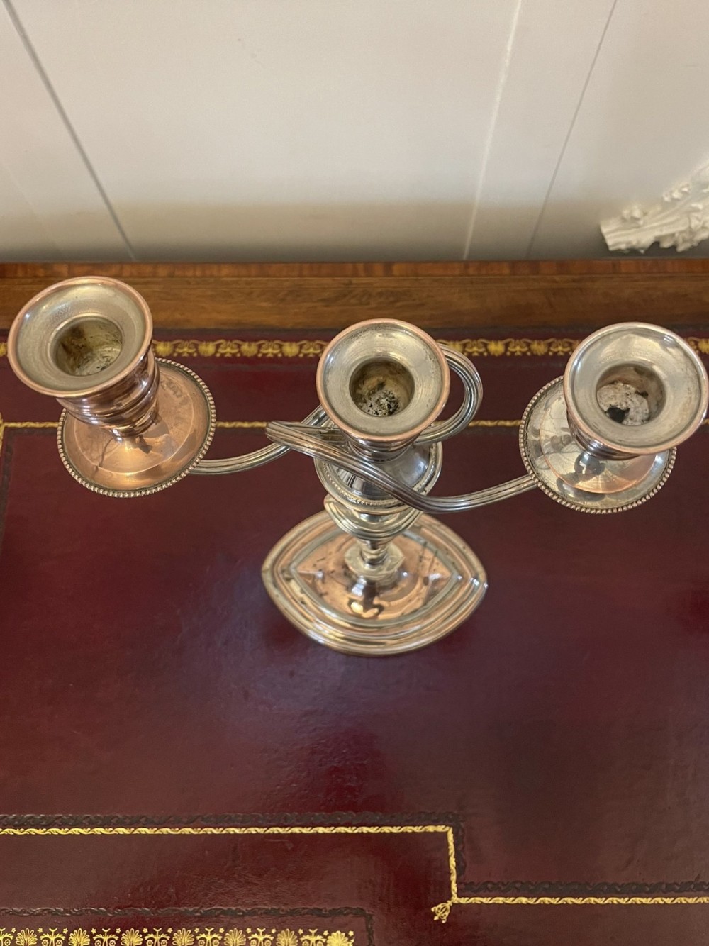 A pair of antique silver-plated three-light candelabras with curved branch arms, tapered baluster stems, and moulded oval bases showing subtle copper undertones. View V