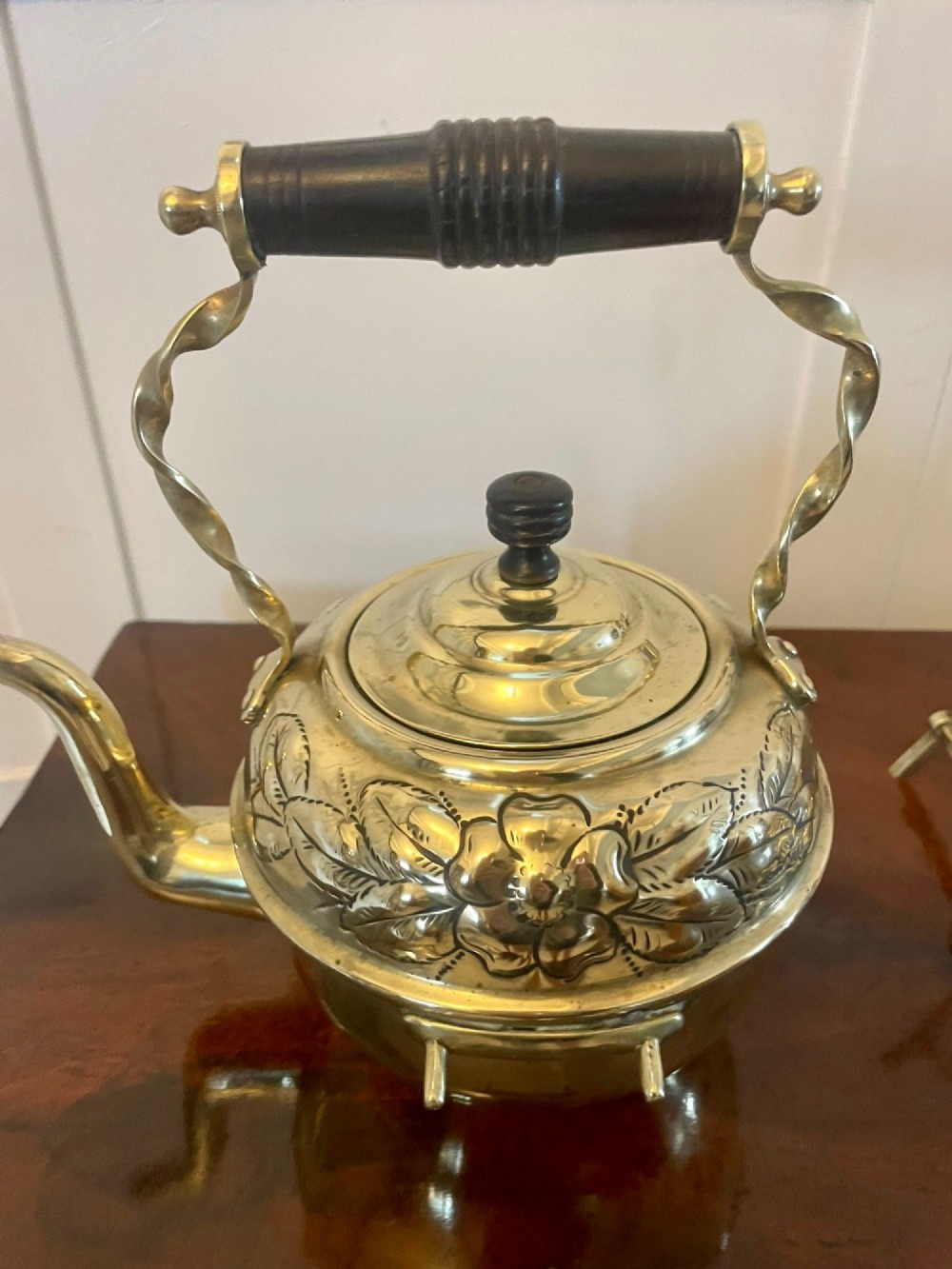 An antique Victorian brass spirit kettle featuring floral engravings, an ebonised wooden handle, and a matching brass stand with a spirit burner. View V