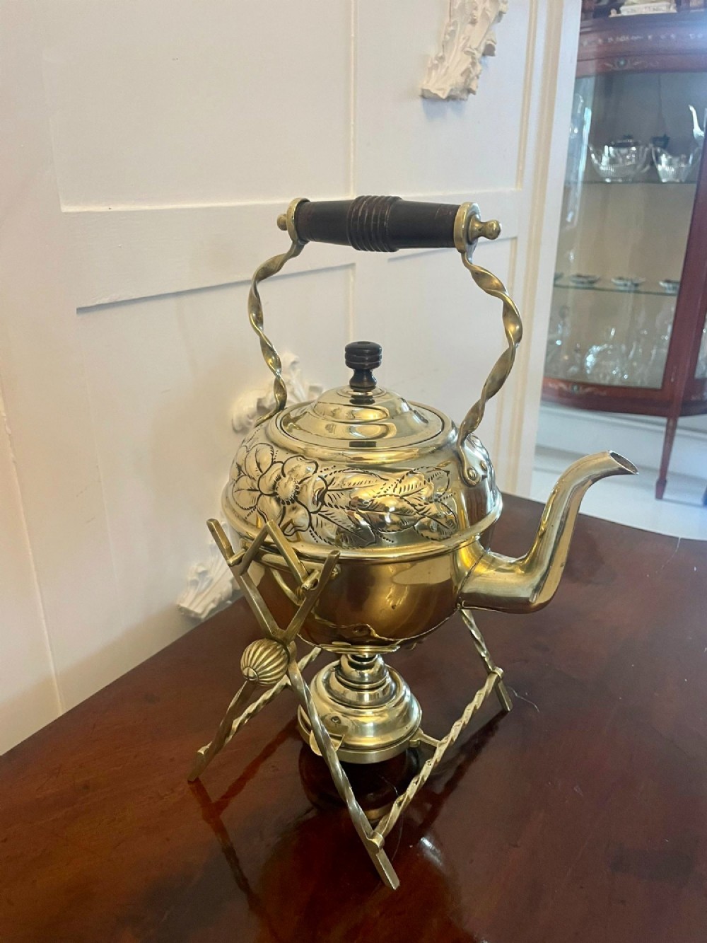 An antique Victorian brass spirit kettle featuring floral engravings, an ebonised wooden handle, and a matching brass stand with a spirit burner. View IX