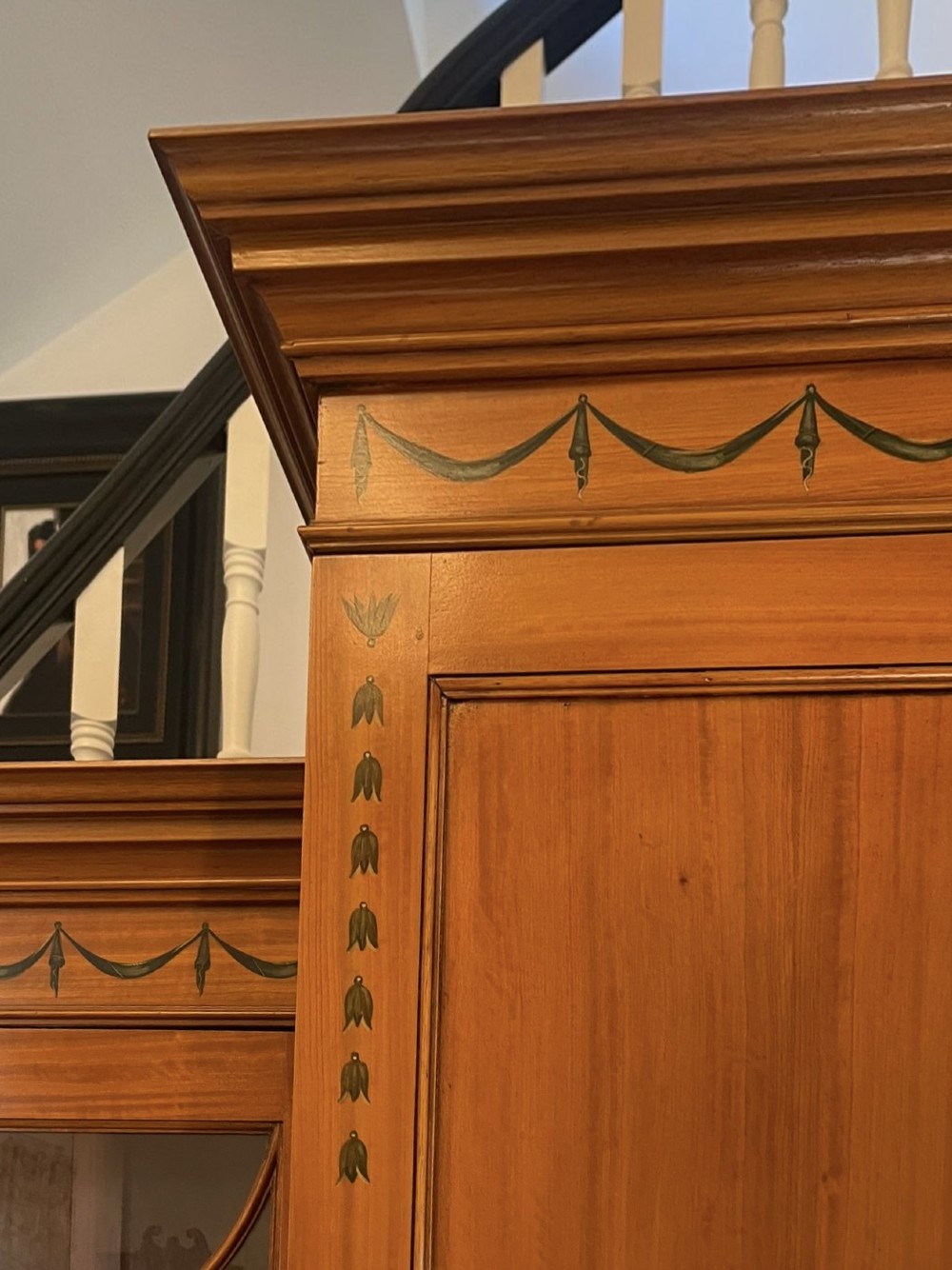 A large satinwood breakfront bookcase featuring hand-painted floral cartouches, upper glazed display doors, and lower cupboard panels. View IX