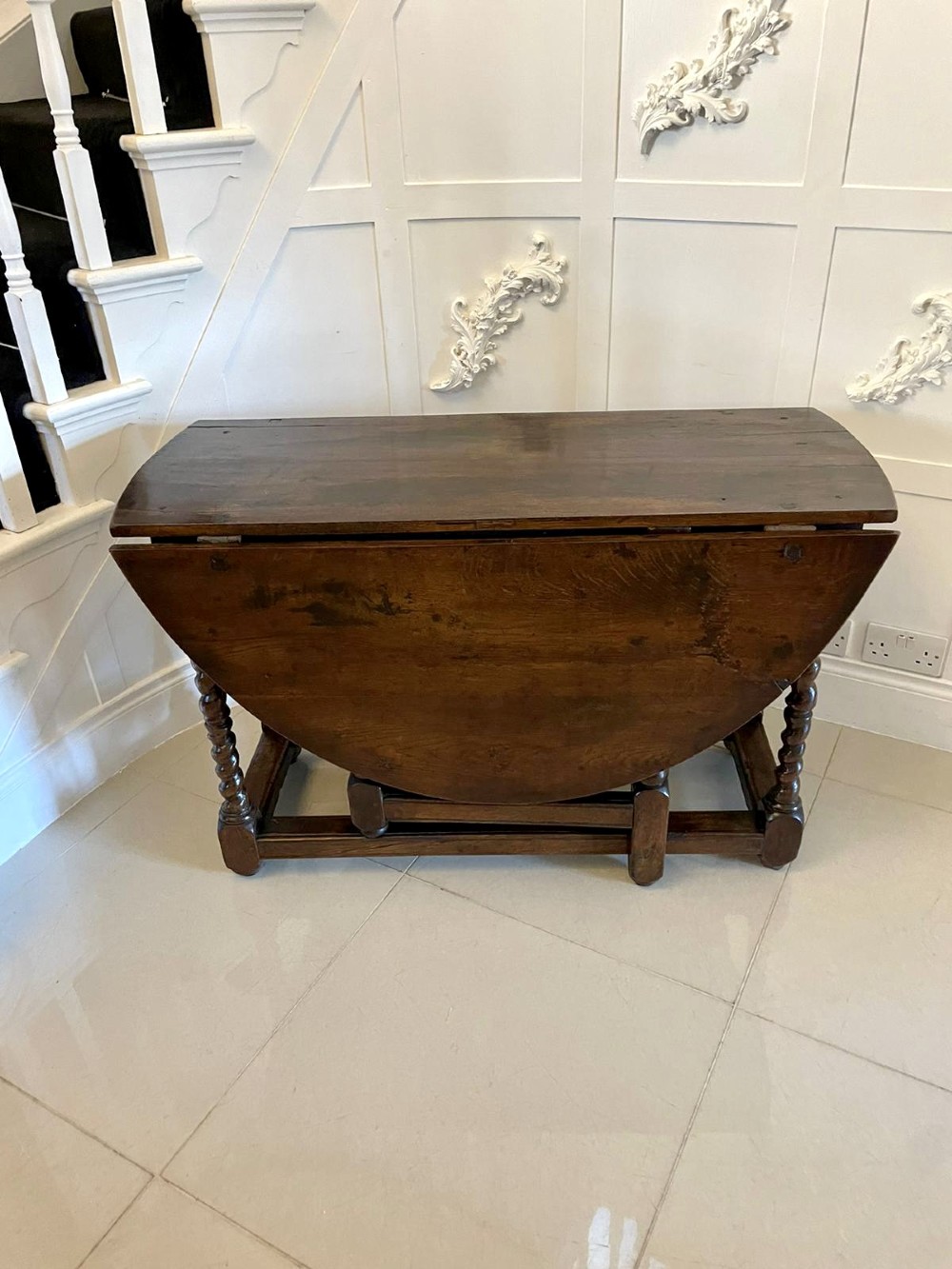 A dark oak seventeenth-century gateleg dining table with folded drop leaves, barley twist legs, and sturdy base stretchers.