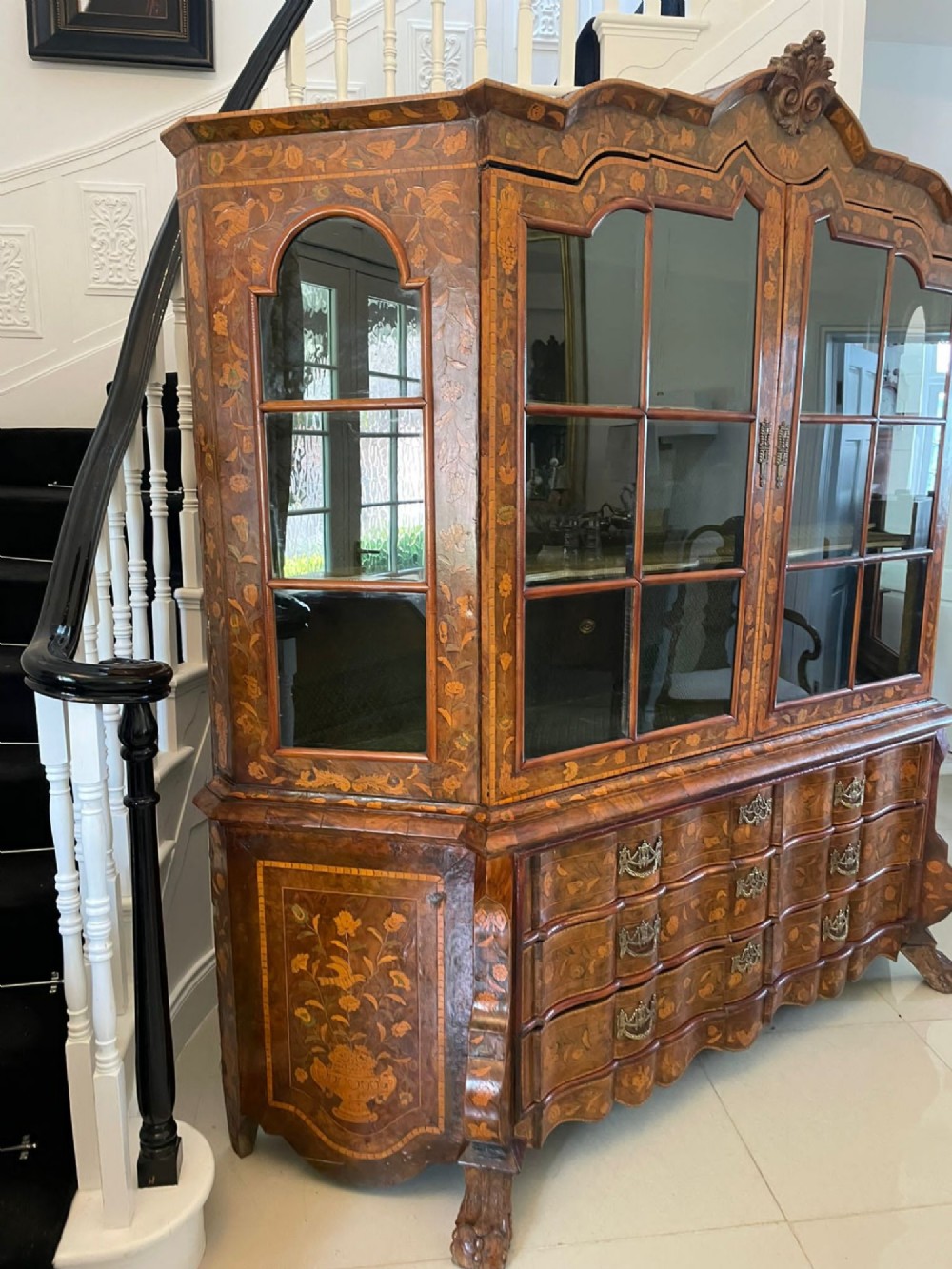 An antique Dutch burr walnut display cabinet featuring elaborate floral marquetry inlay, glazed upper doors, a serpentine three-drawer base, and carved claw feet. View II