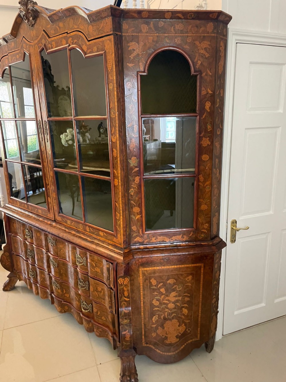 An antique Dutch burr walnut display cabinet featuring elaborate floral marquetry inlay, glazed upper doors, a serpentine three-drawer base, and carved claw feet. View III