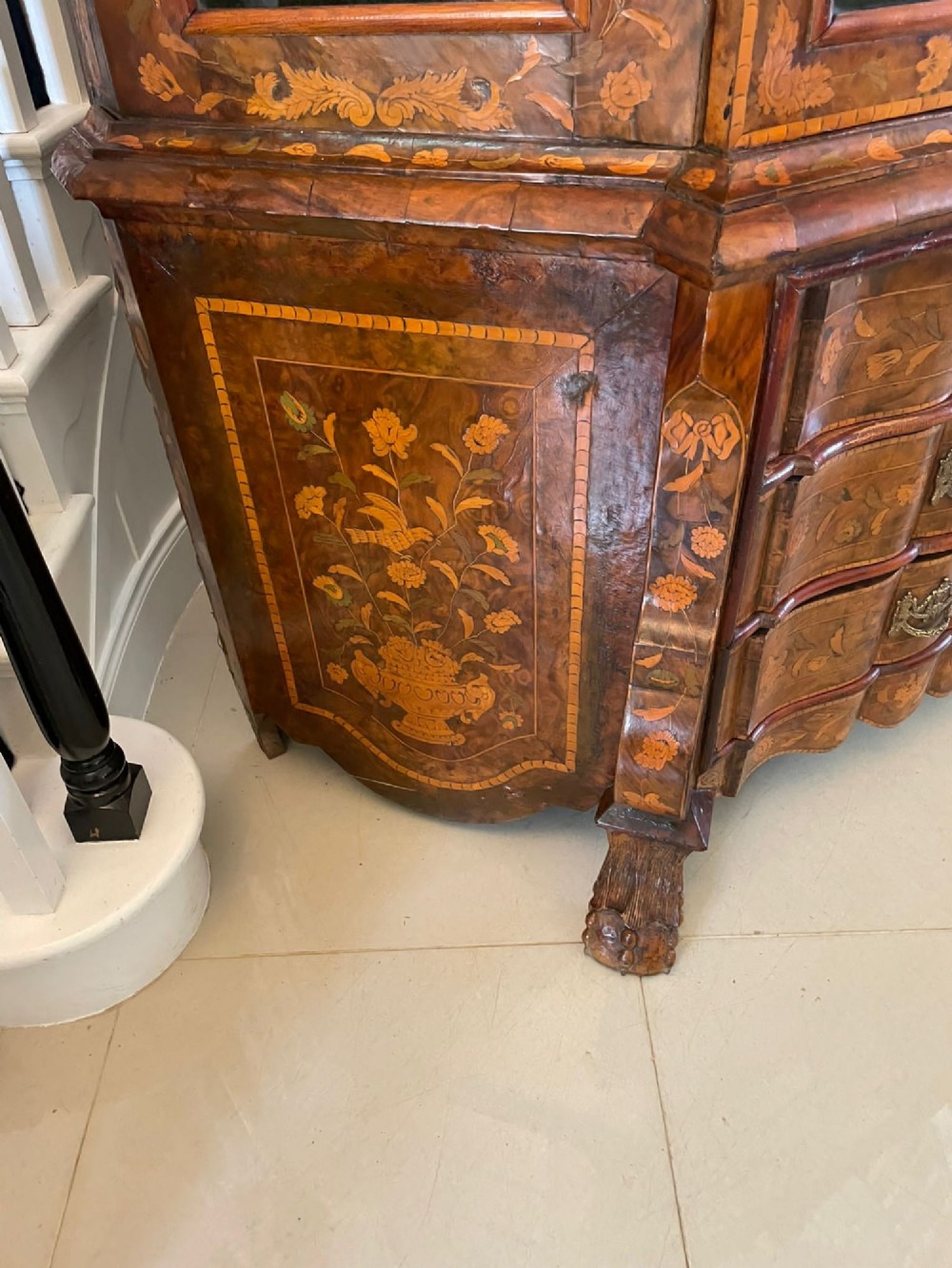 An antique Dutch burr walnut display cabinet featuring elaborate floral marquetry inlay, glazed upper doors, a serpentine three-drawer base, and carved claw feet. View IV