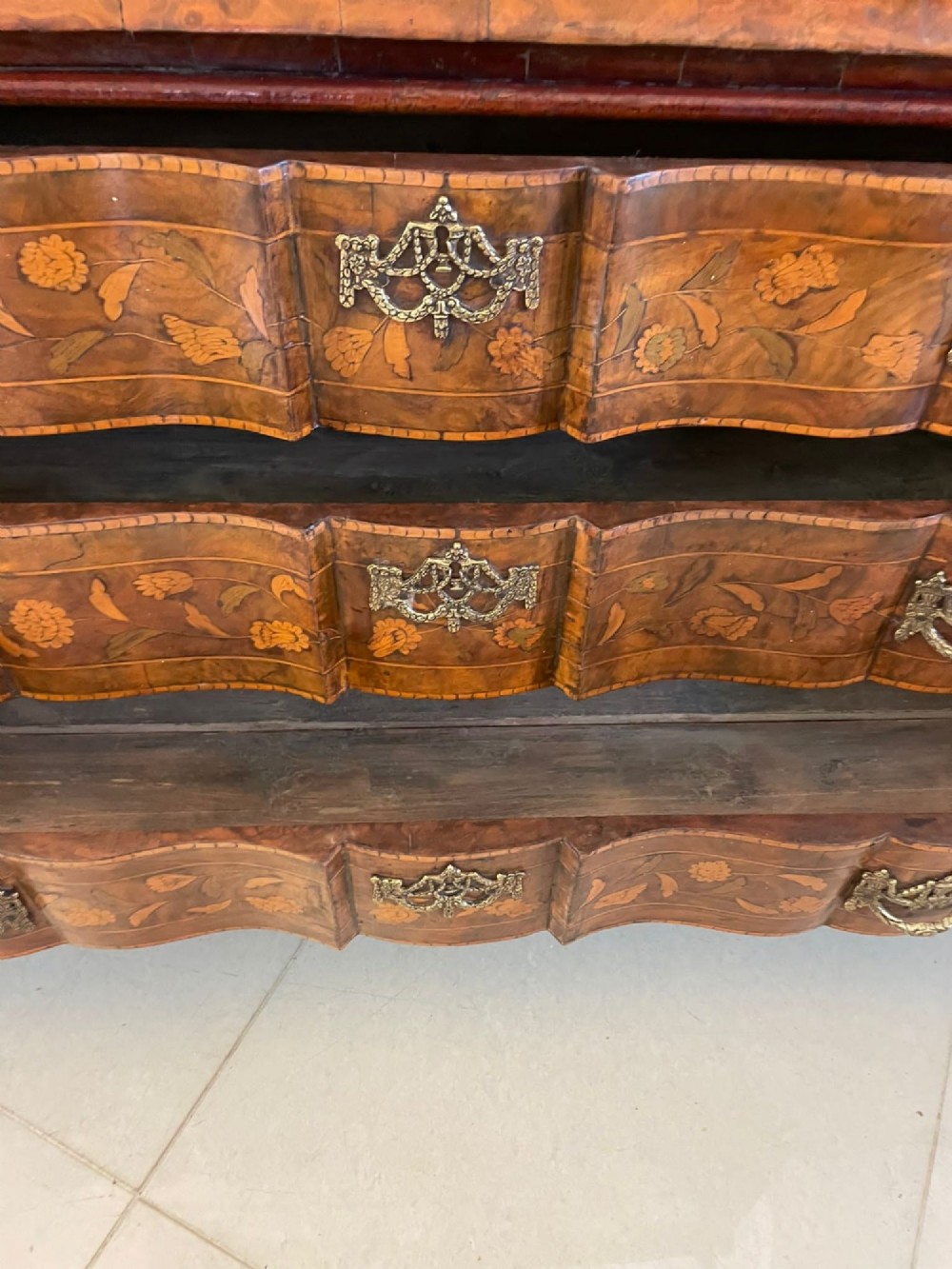 An antique Dutch burr walnut display cabinet featuring elaborate floral marquetry inlay, glazed upper doors, a serpentine three-drawer base, and carved claw feet. View VI