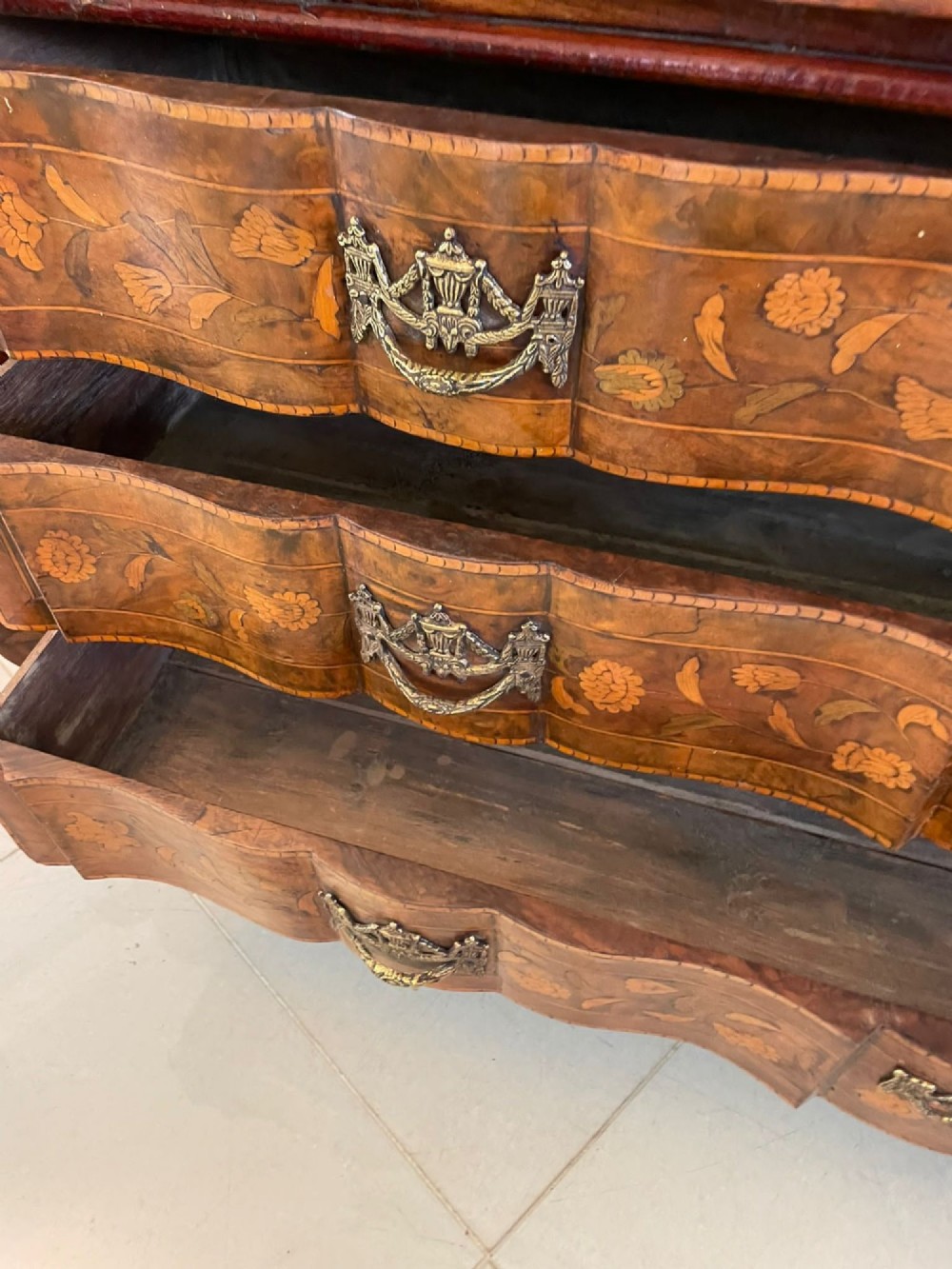 An antique Dutch burr walnut display cabinet featuring elaborate floral marquetry inlay, glazed upper doors, a serpentine three-drawer base, and carved claw feet. View VII