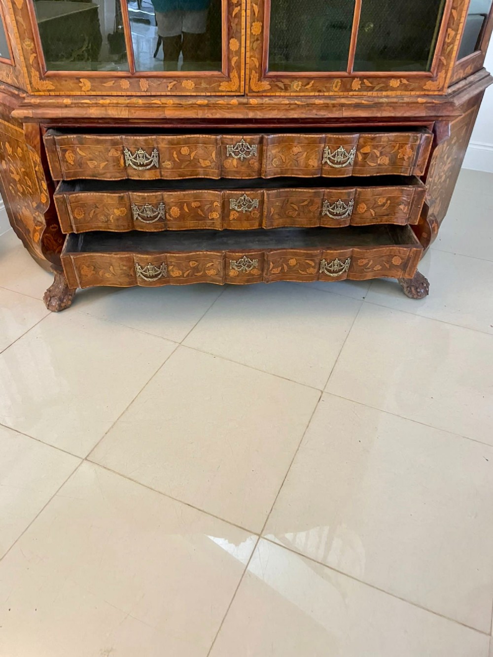 An antique Dutch burr walnut display cabinet featuring elaborate floral marquetry inlay, glazed upper doors, a serpentine three-drawer base, and carved claw feet. View X