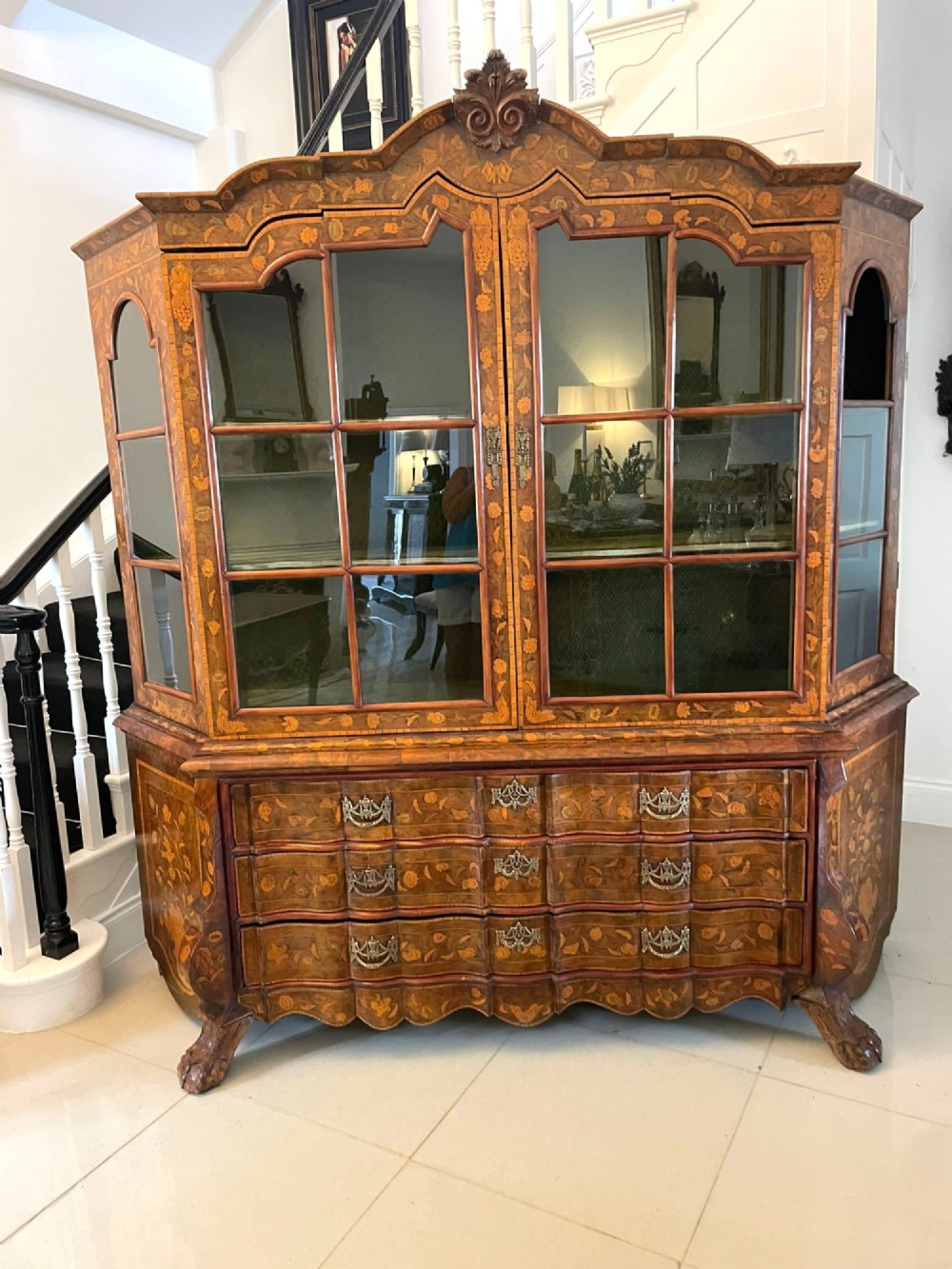 An antique Dutch burr walnut display cabinet featuring elaborate floral marquetry inlay, glazed upper doors, a serpentine three-drawer base, and carved claw feet.