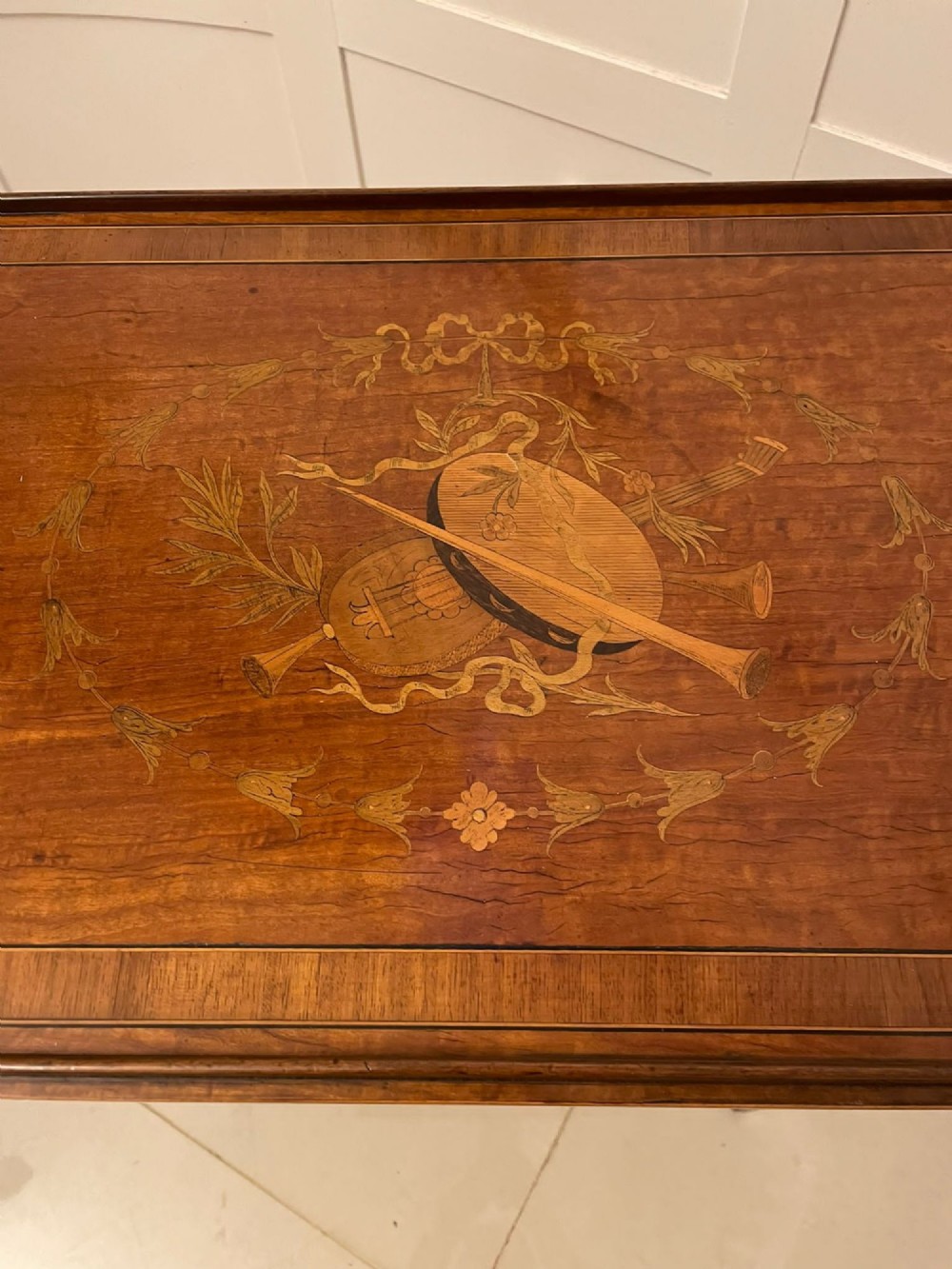 An Edwardian rectangular satinwood inlaid side table featuring a raised tray top with central musical instrument marquetry, slender square tapered legs, and a shaped undertier shelf. View III