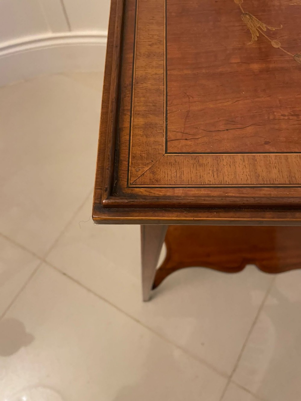 An Edwardian rectangular satinwood inlaid side table featuring a raised tray top with central musical instrument marquetry, slender square tapered legs, and a shaped undertier shelf. View IV