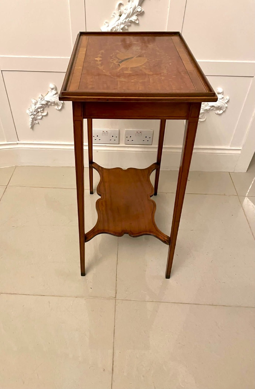 An Edwardian rectangular satinwood inlaid side table featuring a raised tray top with central musical instrument marquetry, slender square tapered legs, and a shaped undertier shelf. View VII