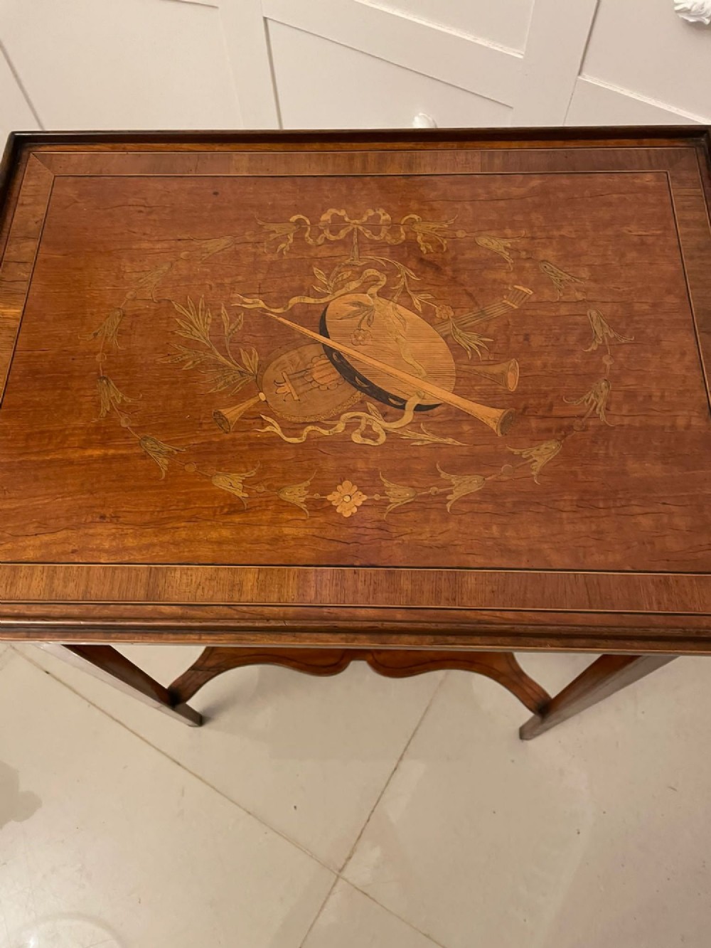 An Edwardian rectangular satinwood inlaid side table featuring a raised tray top with central musical instrument marquetry, slender square tapered legs, and a shaped undertier shelf. View VIII