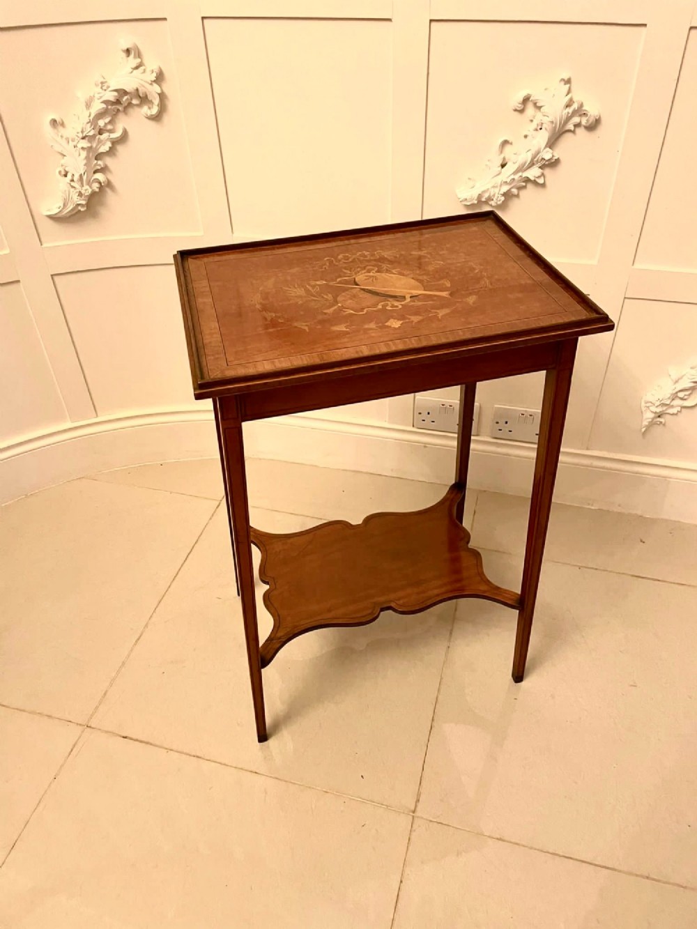 An Edwardian rectangular satinwood inlaid side table featuring a raised tray top with central musical instrument marquetry, slender square tapered legs, and a shaped undertier shelf.