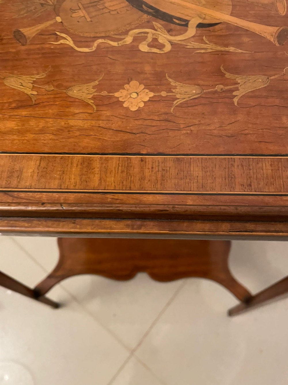 An Edwardian rectangular satinwood inlaid side table featuring a raised tray top with central musical instrument marquetry, slender square tapered legs, and a shaped undertier shelf. View IX