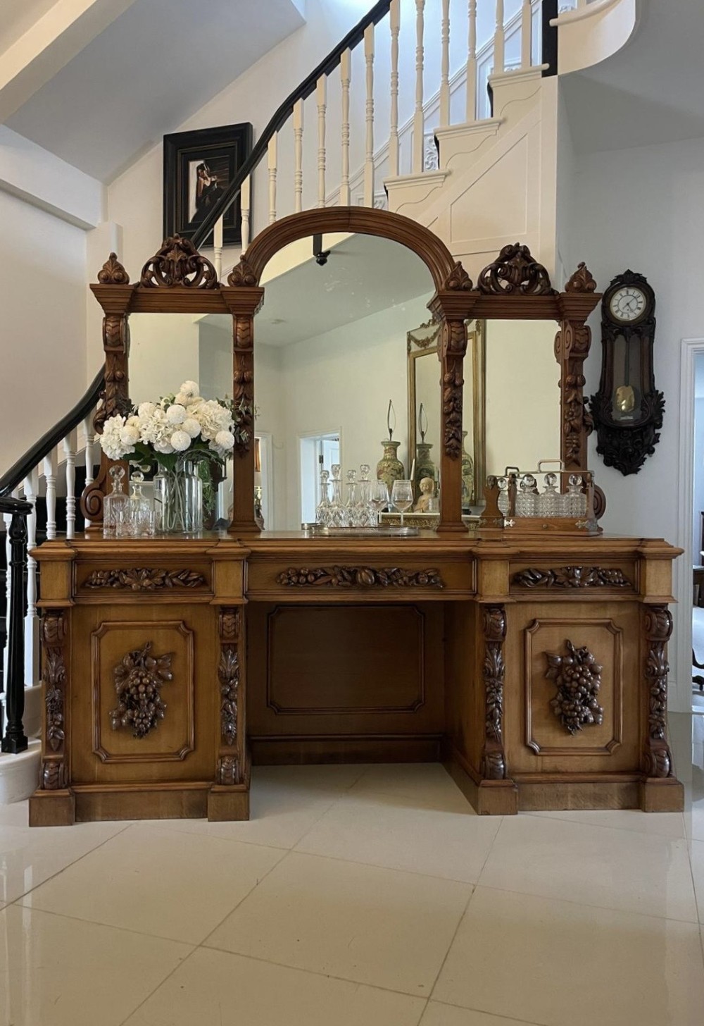 A large Victorian carved oak sideboard featuring three upper mirror panels, intricate grape cluster wood carvings, and a pedestal base. View VI