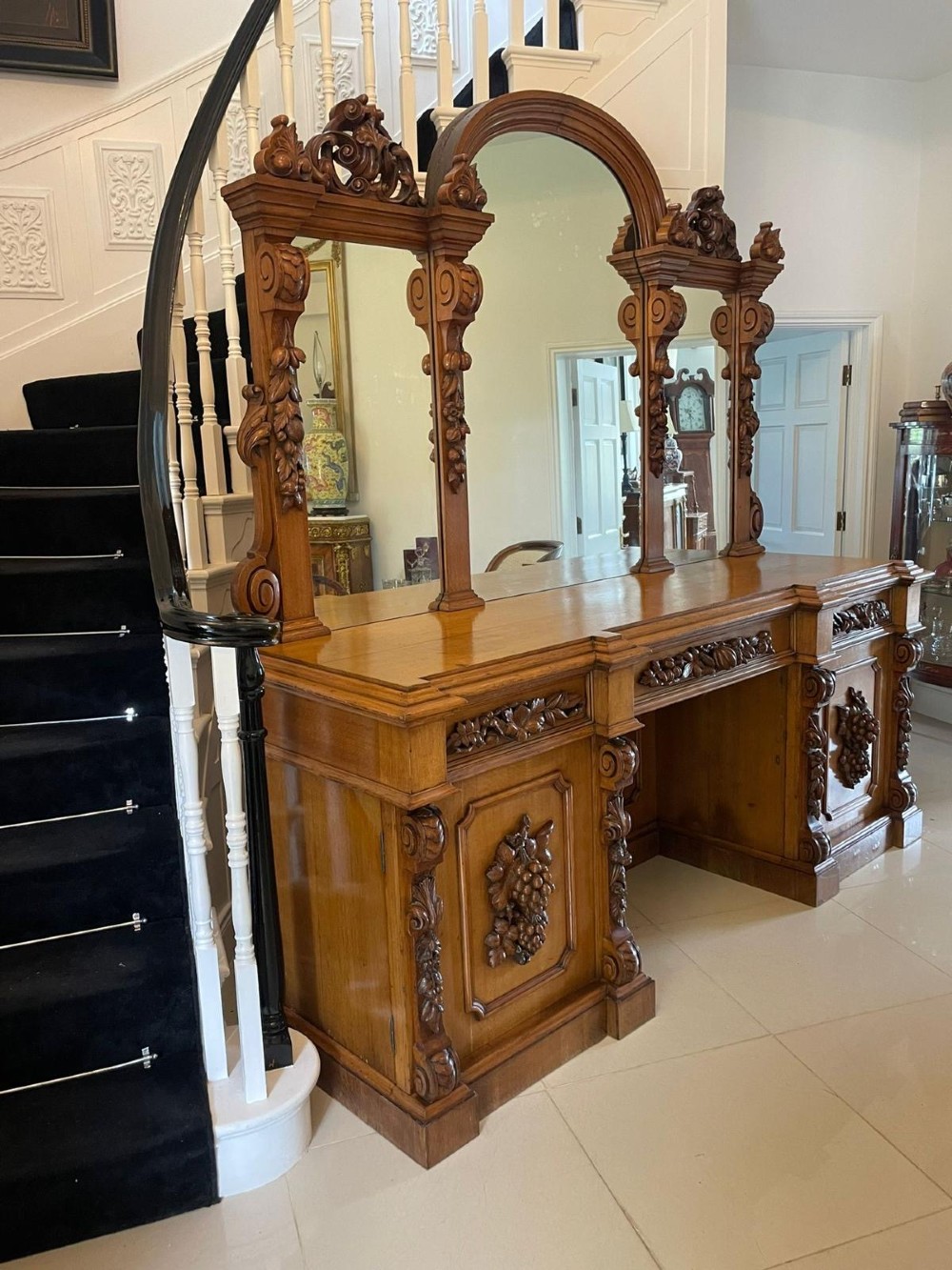 A large Victorian carved oak sideboard featuring three upper mirror panels, intricate grape cluster wood carvings, and a pedestal base. View VIII