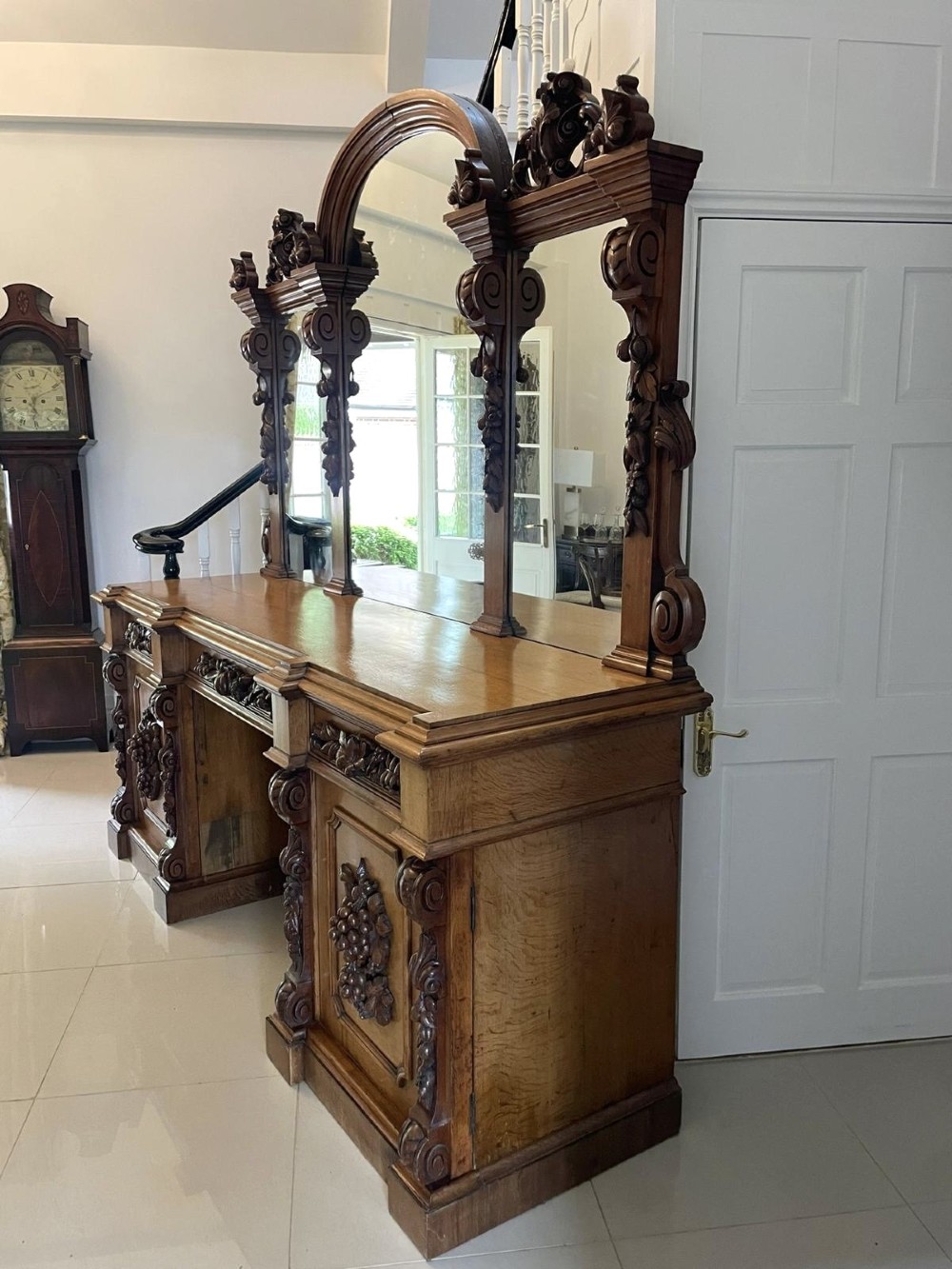 A large Victorian carved oak sideboard featuring three upper mirror panels, intricate grape cluster wood carvings, and a pedestal base. View IX