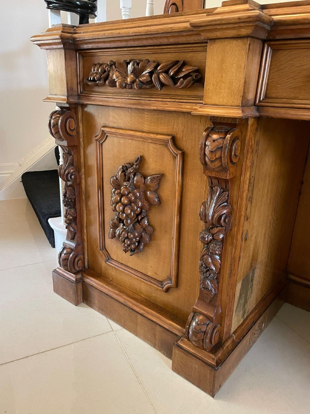 A large Victorian carved oak sideboard featuring three upper mirror panels, intricate grape cluster wood carvings, and a pedestal base. View XII