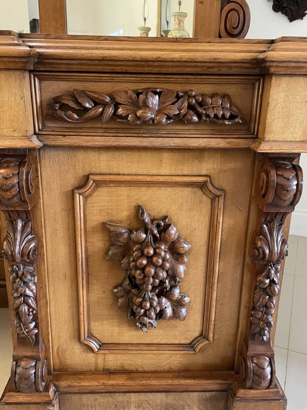 A large Victorian carved oak sideboard featuring three upper mirror panels, intricate grape cluster wood carvings, and a pedestal base. View XIII