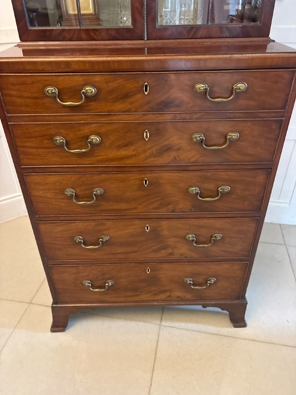 A tall Georgian mahogany secretaire bookcase featuring an upper cabinet with astragal glazed doors and a lower chest of drawers with brass handles. View V