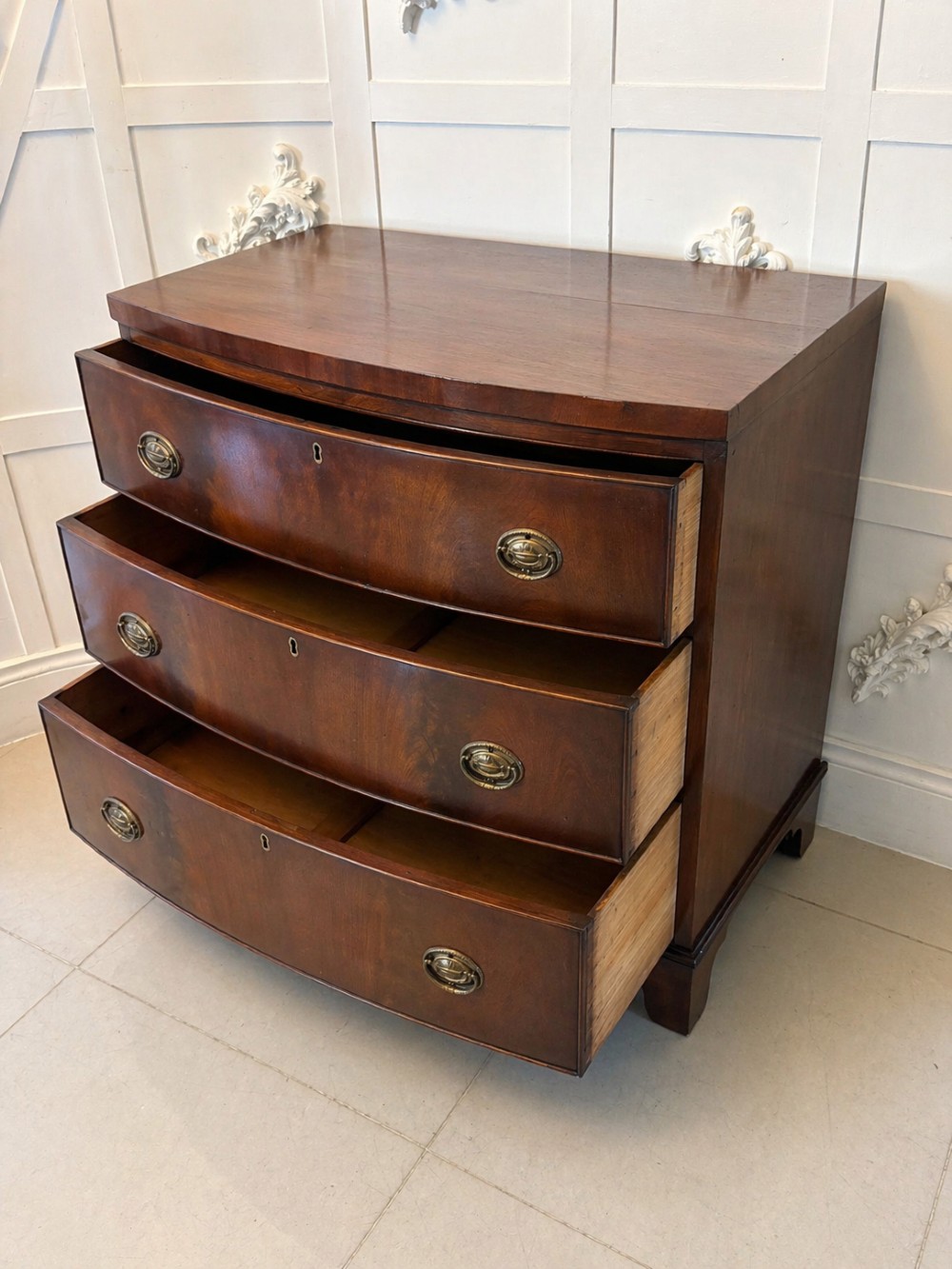A Georgian mahogany bow-front chest of three drawers featuring oval brass drop handles and raised on bracket feet. View VI