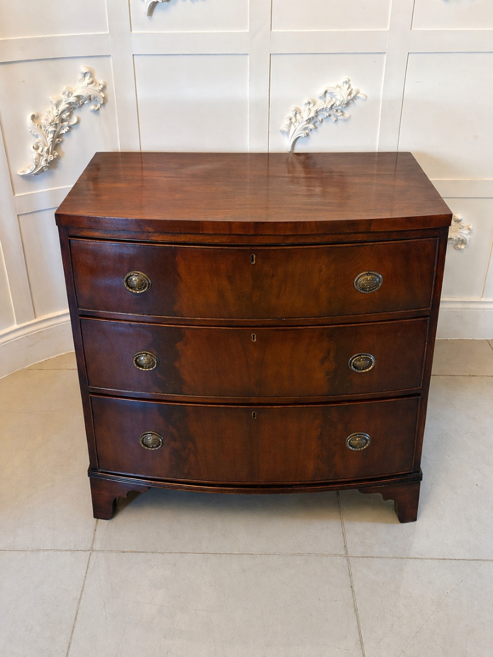 A Georgian mahogany bow-front chest of three drawers featuring oval brass drop handles and raised on bracket feet. View VII