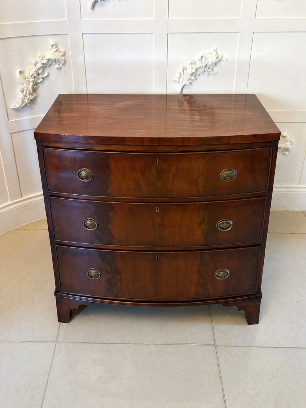 A Georgian mahogany bow-front chest of three drawers featuring oval brass drop handles and raised on bracket feet. View VIII