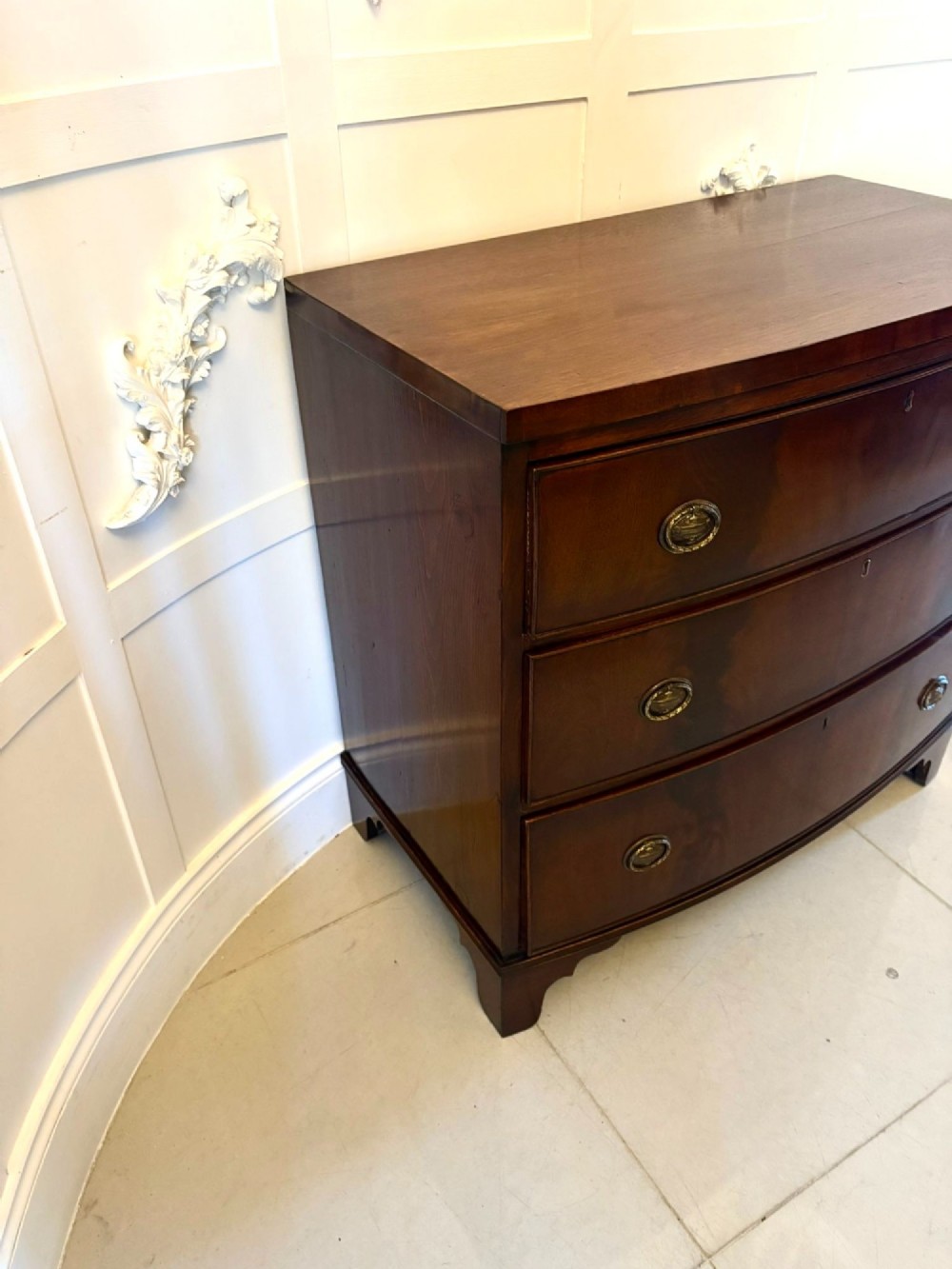 A Georgian mahogany bow-front chest of three drawers featuring oval brass drop handles and raised on bracket feet. View IX