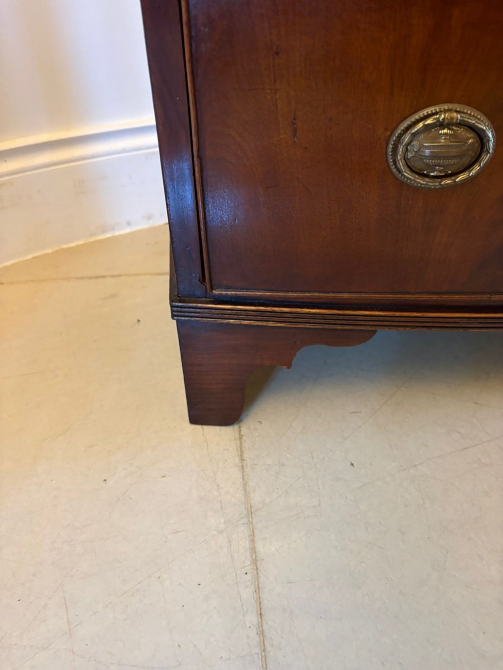 A Georgian mahogany bow-front chest of three drawers featuring oval brass drop handles and raised on bracket feet. View X