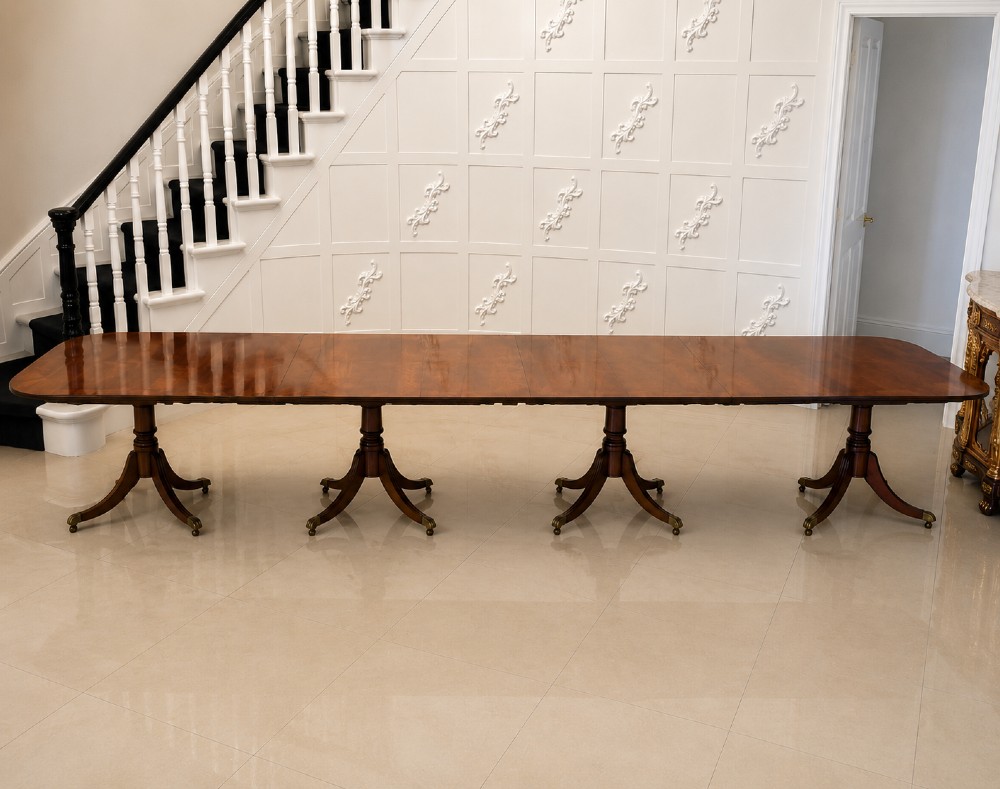 A long extendable mahogany banquet dining table set on four turned pedestal bases with splayed legs and brass castors.