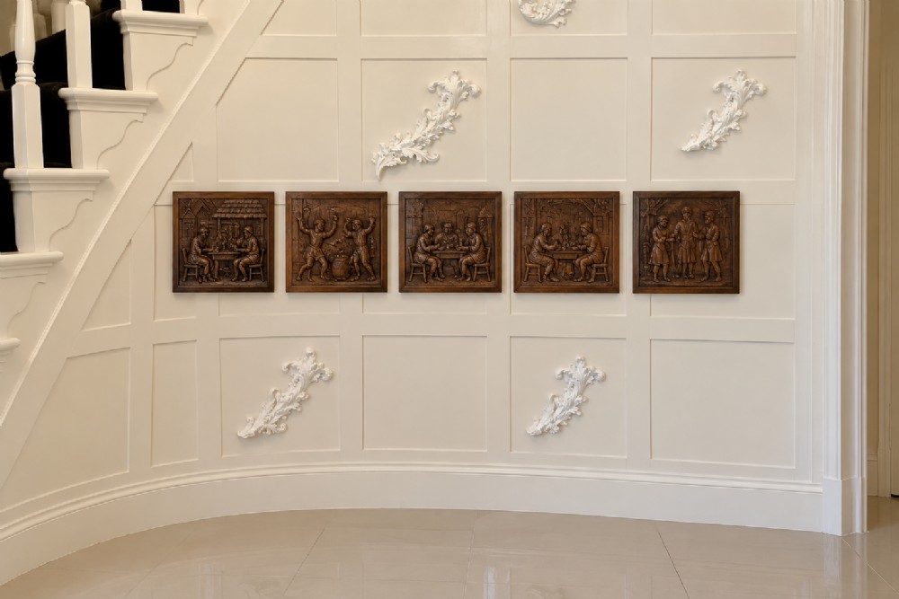 A set of five square dark carved oak wall panels featuring detailed bas-relief scenes of figures in traditional Flemish tavern settings.