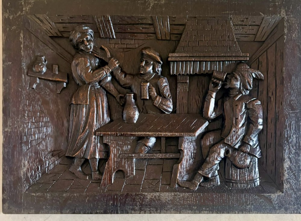 A set of five square dark carved oak wall panels featuring detailed bas-relief scenes of figures in traditional Flemish tavern settings. View III
