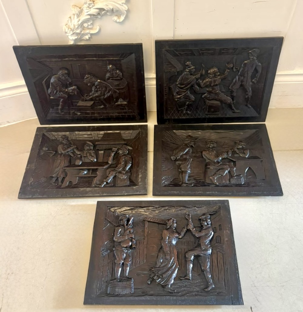 A set of five square dark carved oak wall panels featuring detailed bas-relief scenes of figures in traditional Flemish tavern settings. View VI