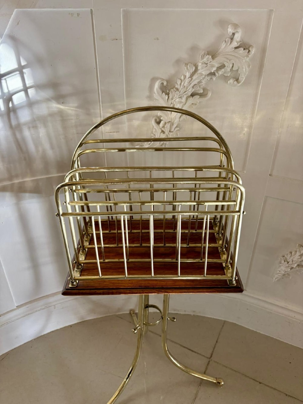 An antique Victorian brass magazine rack with divided wire compartments set upon a polished rectangular oak base and a curved brass tripod stand. View II