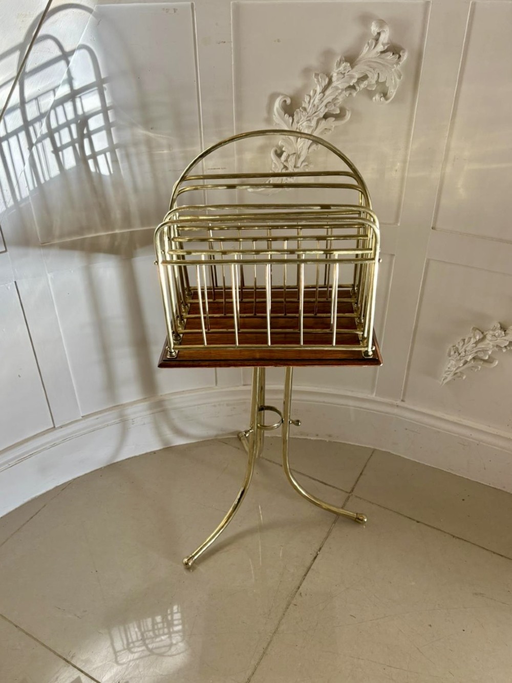 An antique Victorian brass magazine rack with divided wire compartments set upon a polished rectangular oak base and a curved brass tripod stand.