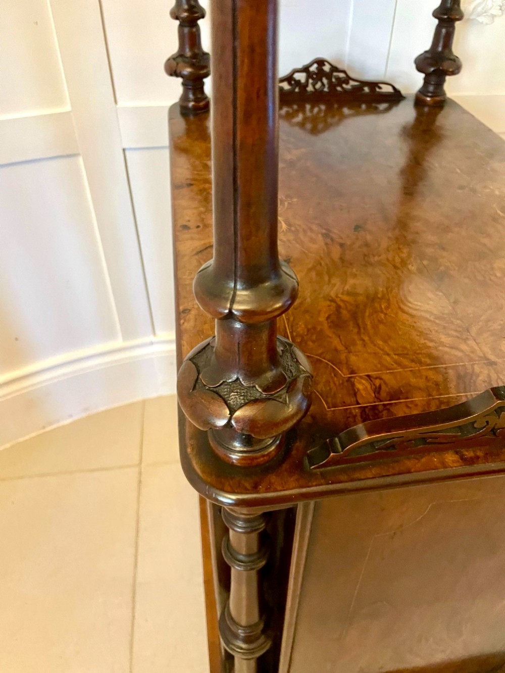 An antique Victorian burr walnut music cabinet featuring two open upper shelves supported by turned columns and a lower glass-fronted cupboard with gold lettered divisions on castors. View VII