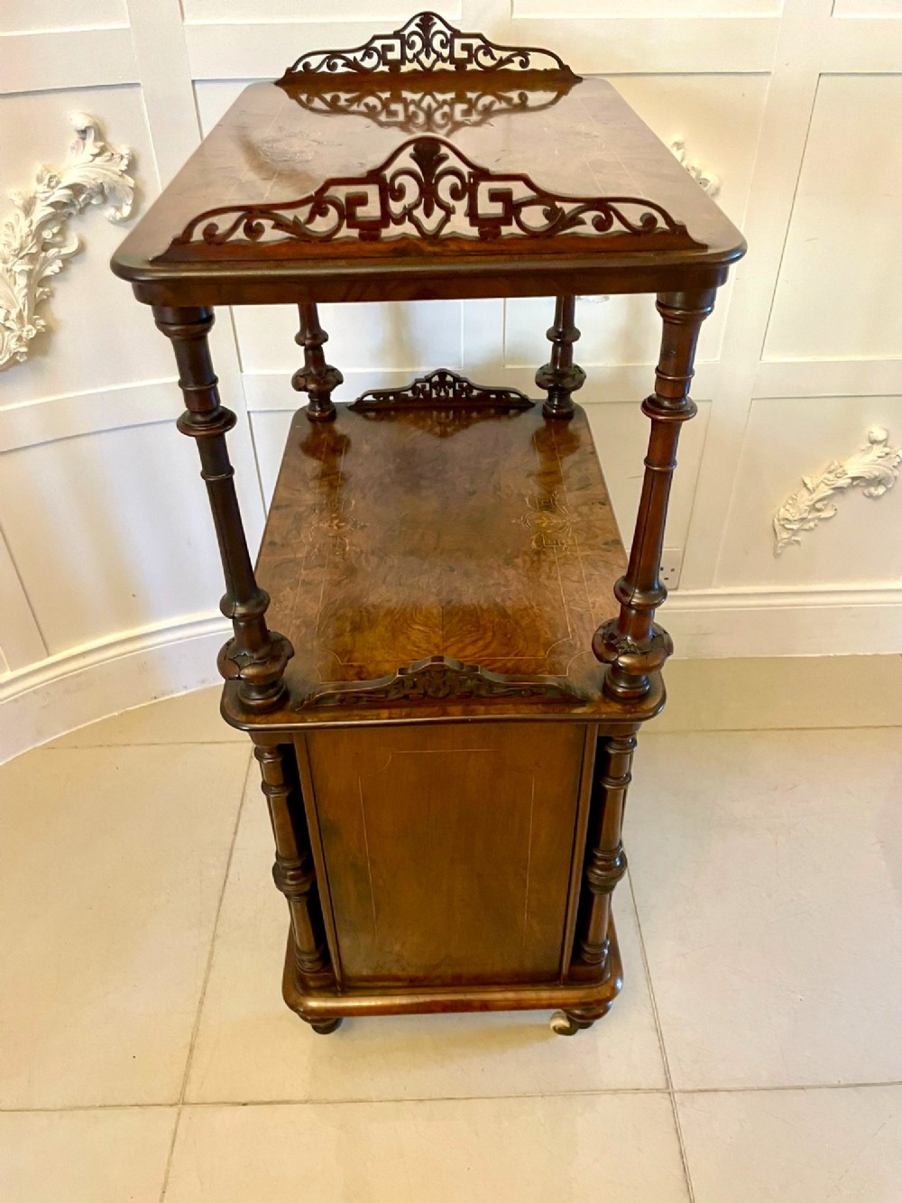 An antique Victorian burr walnut music cabinet featuring two open upper shelves supported by turned columns and a lower glass-fronted cupboard with gold lettered divisions on castors. View VIII
