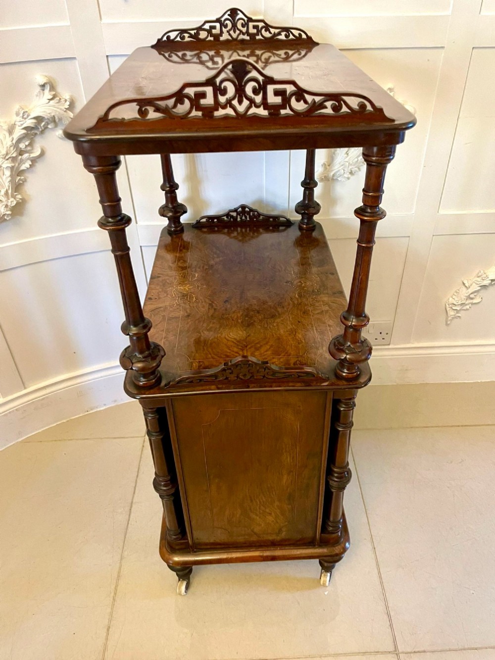 An antique Victorian burr walnut music cabinet featuring two open upper shelves supported by turned columns and a lower glass-fronted cupboard with gold lettered divisions on castors. View IX