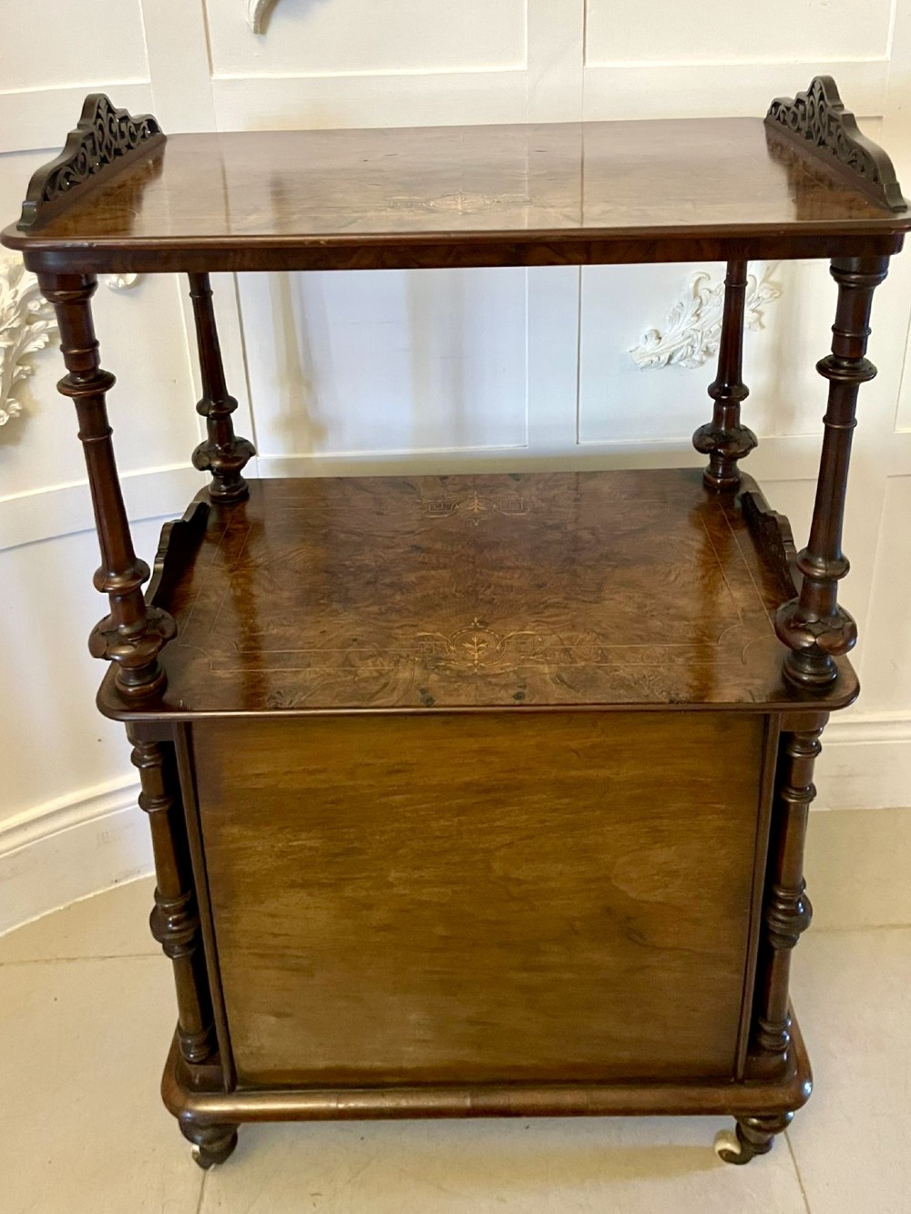 An antique Victorian burr walnut music cabinet featuring two open upper shelves supported by turned columns and a lower glass-fronted cupboard with gold lettered divisions on castors. View XI