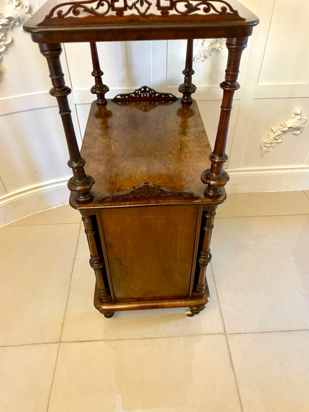 An antique Victorian burr walnut music cabinet featuring two open upper shelves supported by turned columns and a lower glass-fronted cupboard with gold lettered divisions on castors. View XII