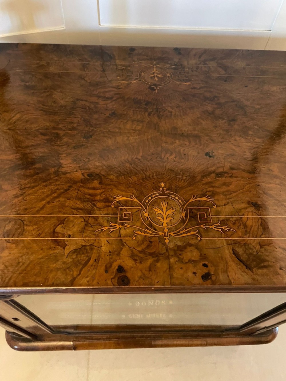 An antique Victorian burr walnut music cabinet featuring two open upper shelves supported by turned columns and a lower glass-fronted cupboard with gold lettered divisions on castors. View XIII
