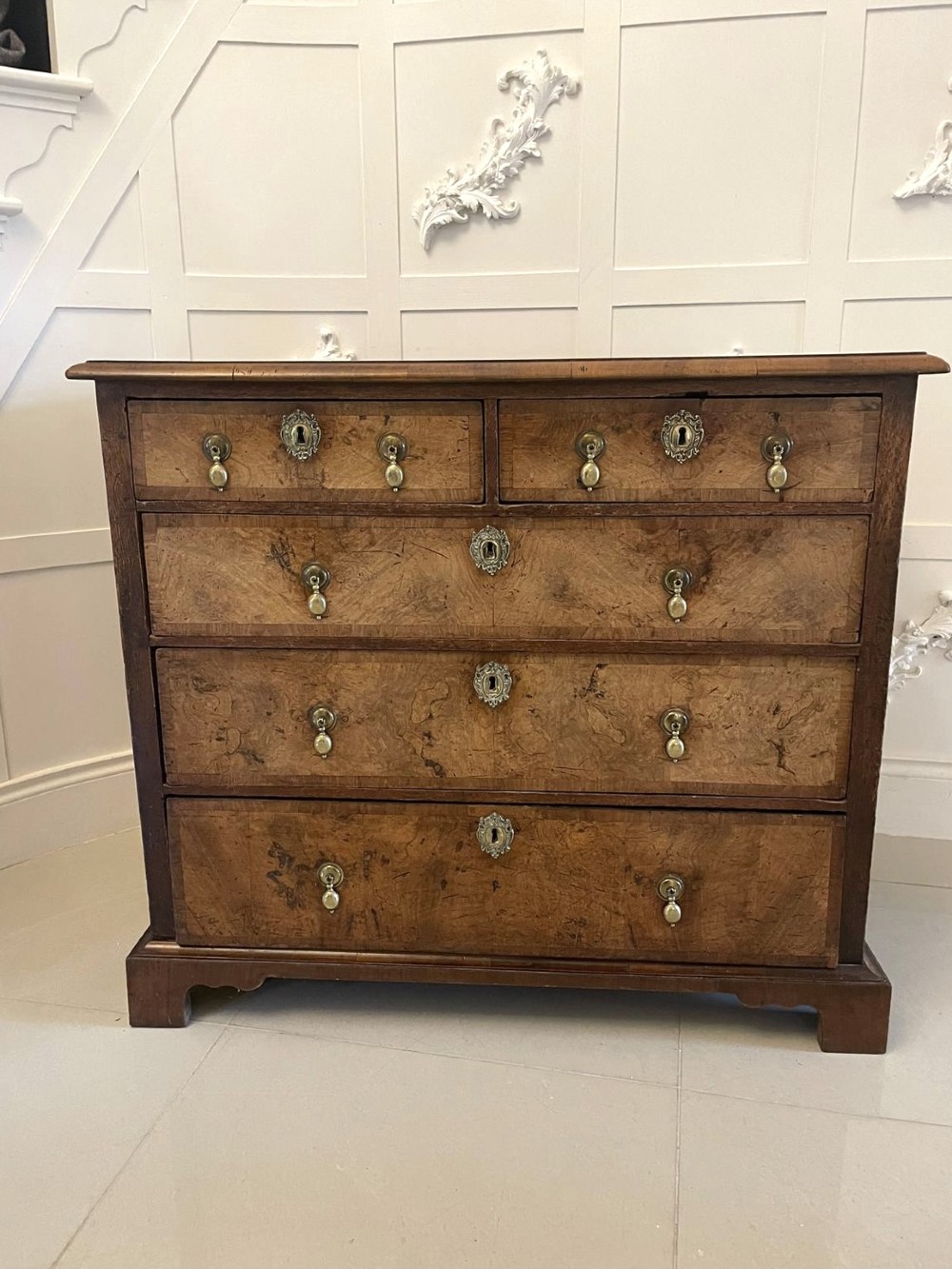 An early 18th-century George I walnut chest of drawers featuring burr walnut veneers, brass drop handles, keyhole escutcheons, and bracket feet. View V
