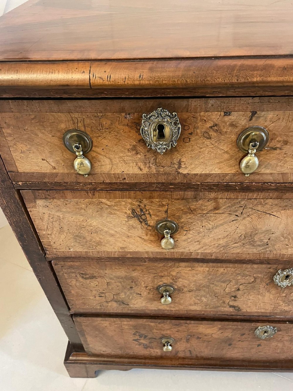 An early 18th-century George I walnut chest of drawers featuring burr walnut veneers, brass drop handles, keyhole escutcheons, and bracket feet. View VIII