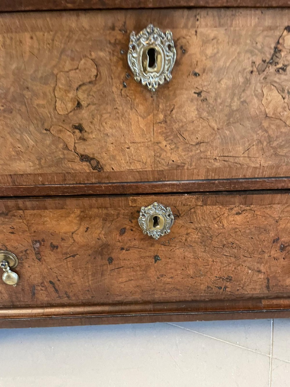 An early 18th-century George I walnut chest of drawers featuring burr walnut veneers, brass drop handles, keyhole escutcheons, and bracket feet. View X