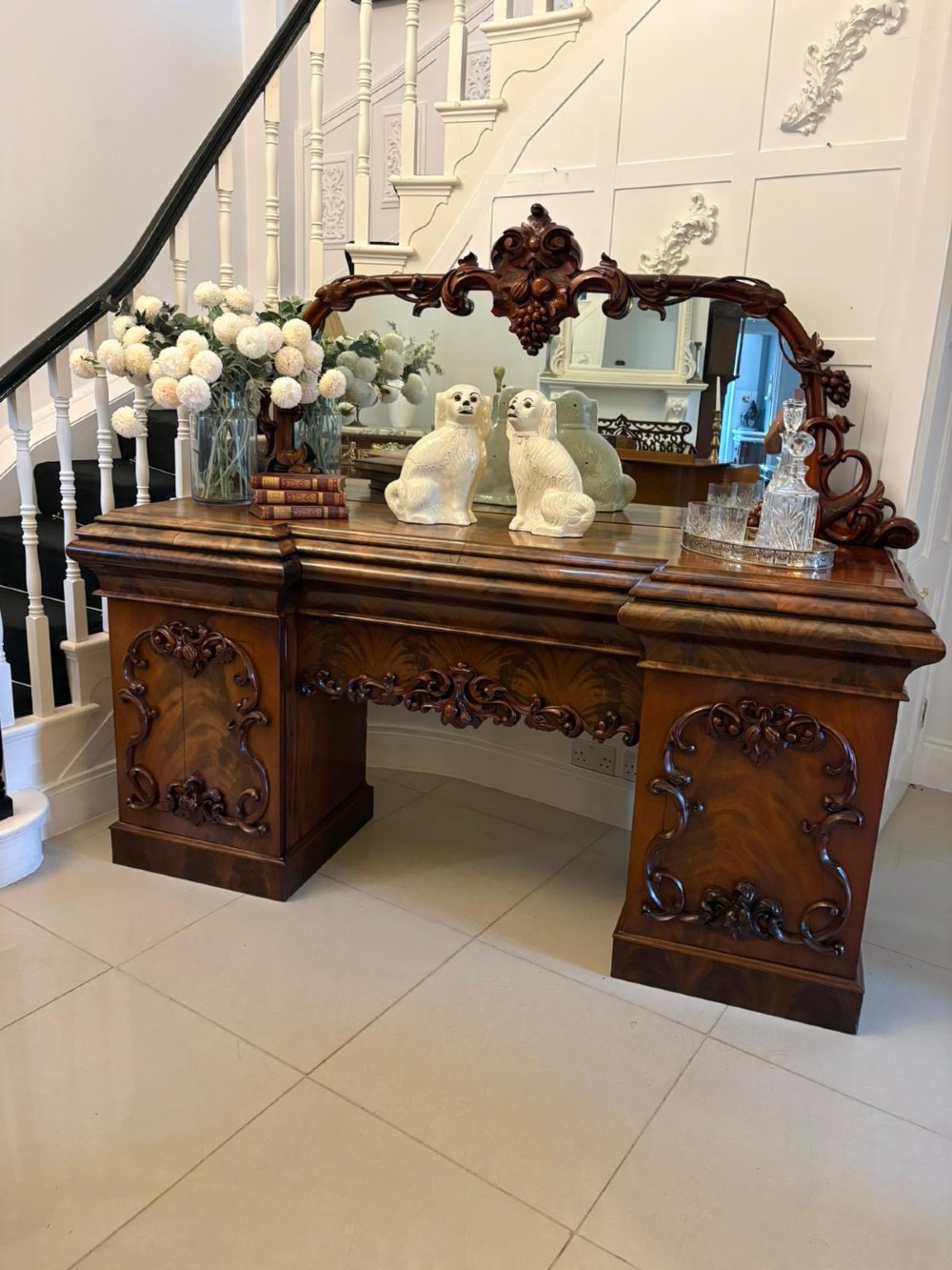 An antique Victorian carved mahogany sideboard featuring twin pedestal bases with carved scroll mouldings and a large arched mirror-backed top frame. View II