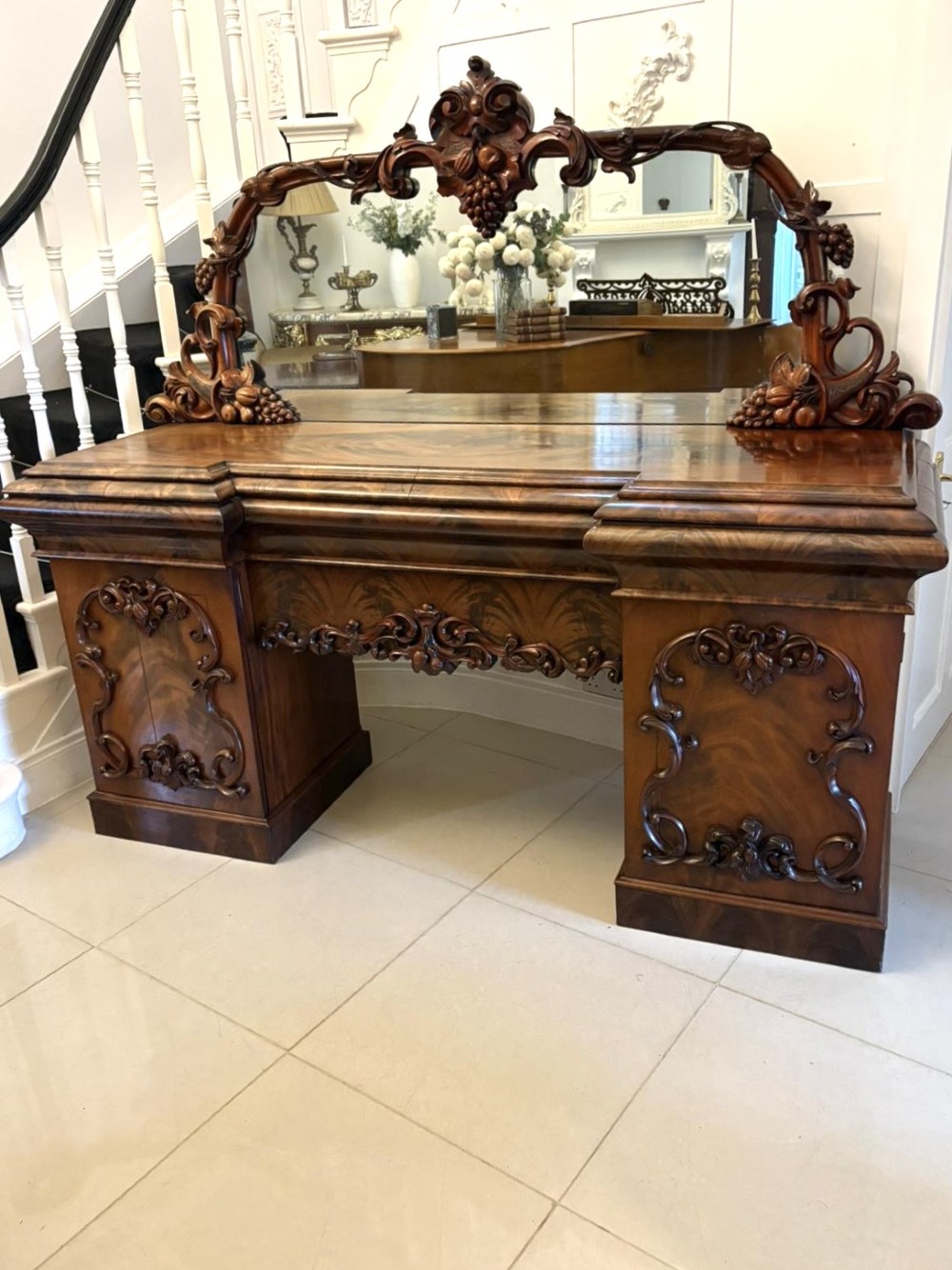 An antique Victorian carved mahogany sideboard featuring twin pedestal bases with carved scroll mouldings and a large arched mirror-backed top frame.