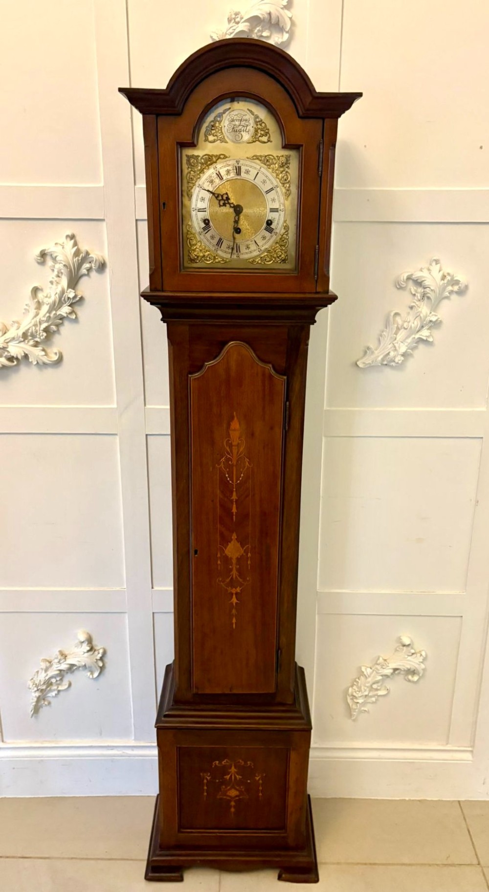 An Edwardian mahogany longcase clock with satinwood urn inlay on the door and a brass dial with Tempus Fugit inscription.