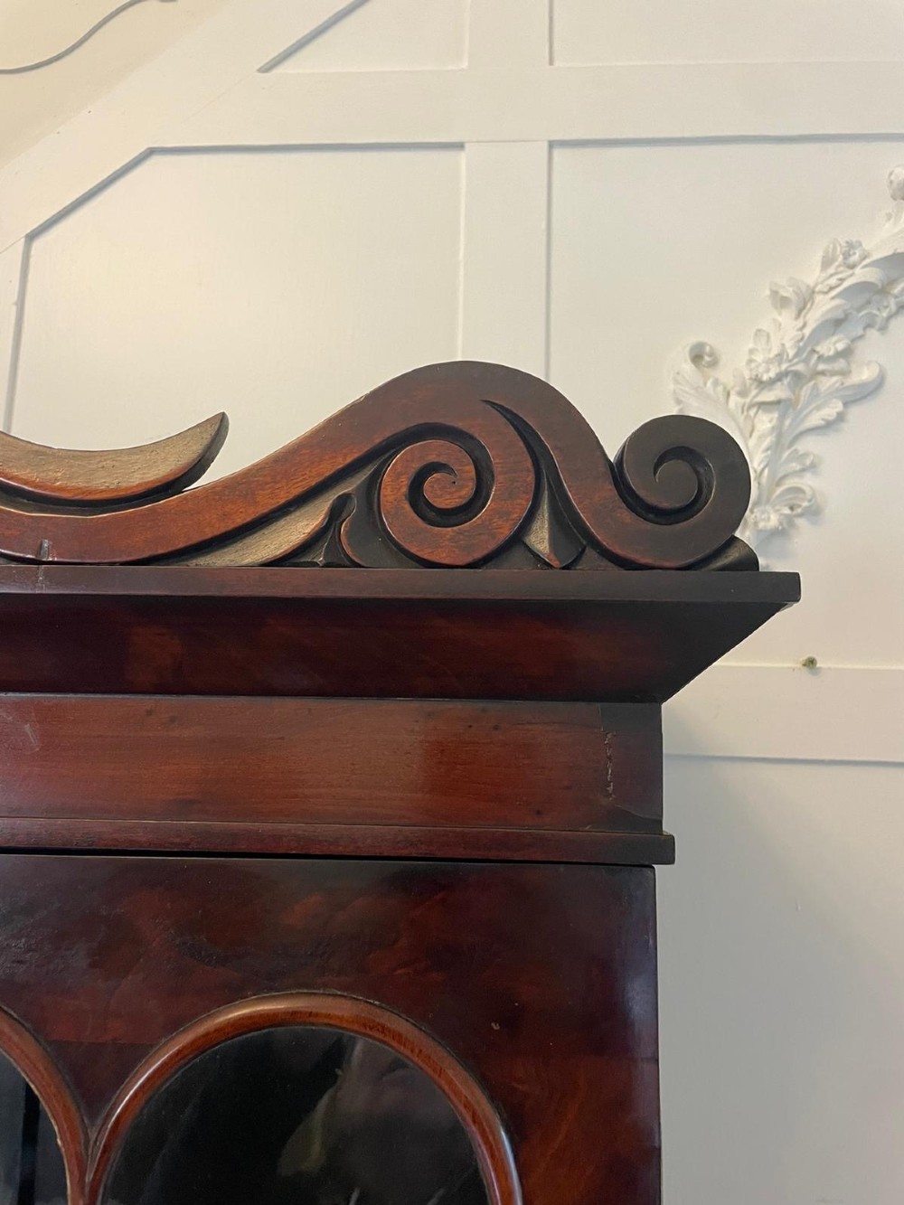 An antique Regency mahogany secretaire bookcase featuring a carved scroll pediment, glazed upper doors, a fall-front desk drawer, and a lower two-door cupboard. View VII