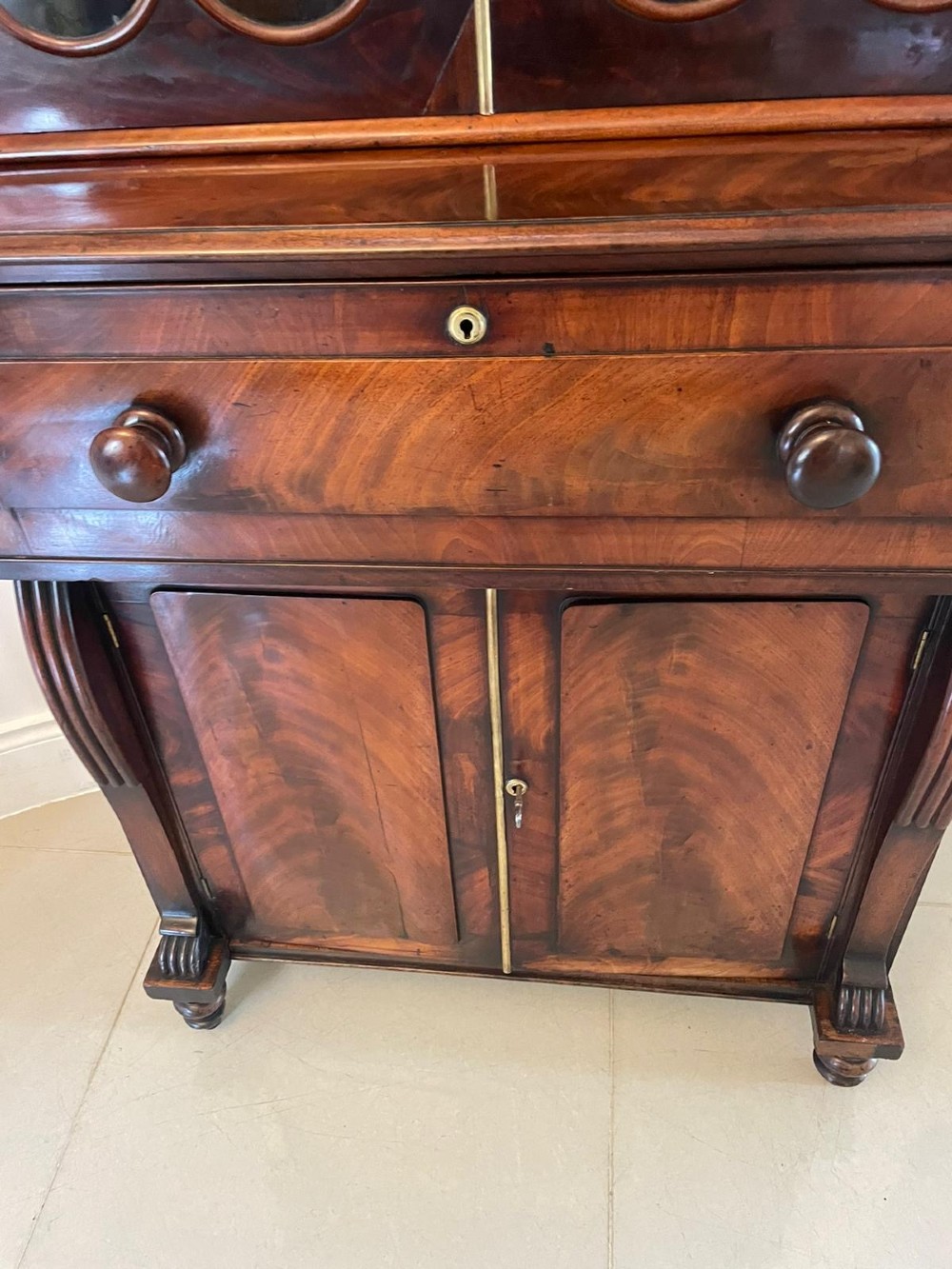 An antique Regency mahogany secretaire bookcase featuring a carved scroll pediment, glazed upper doors, a fall-front desk drawer, and a lower two-door cupboard. View X